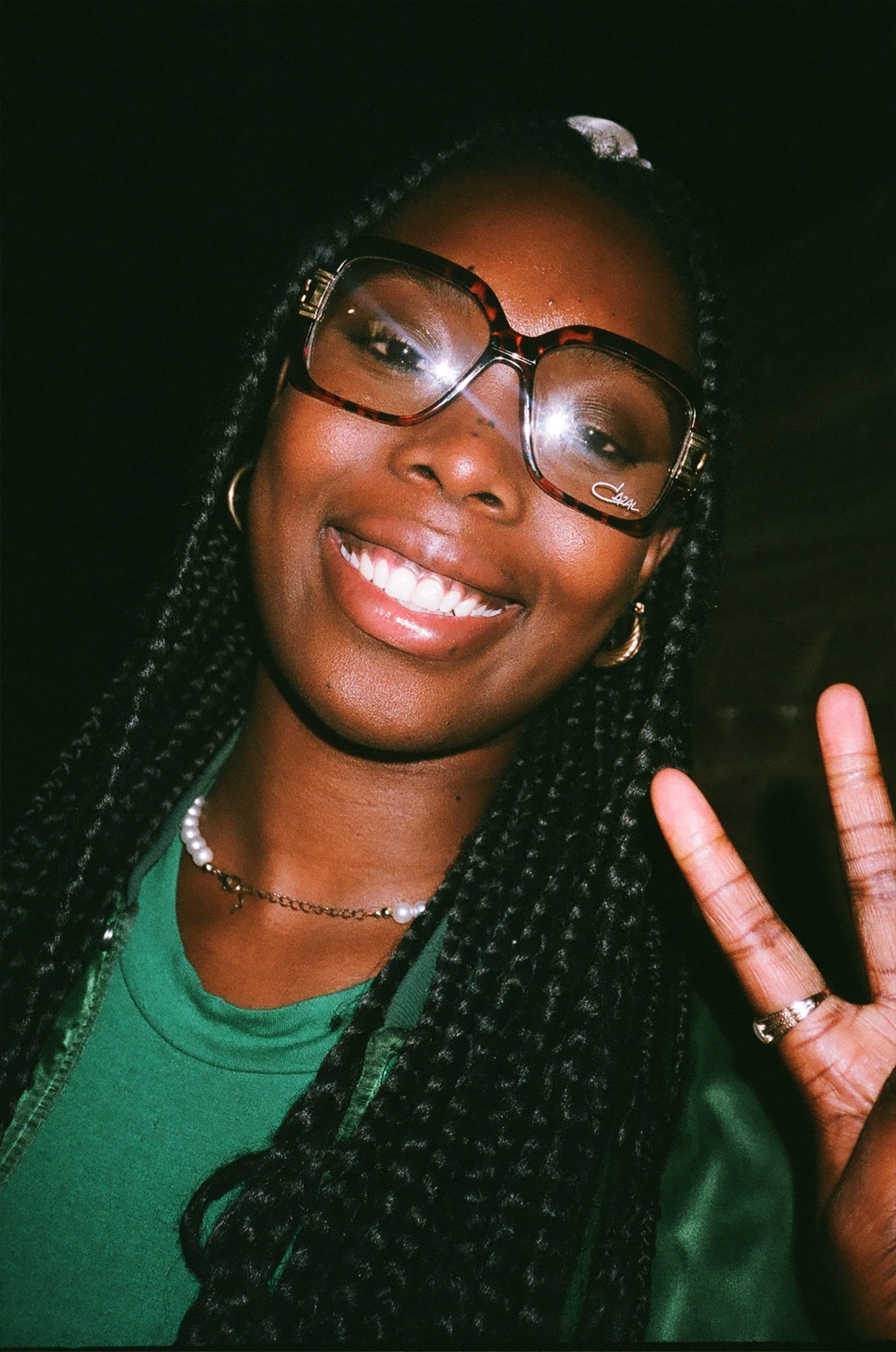 a girl with braids and glasses smiles and throws up a peace sign to camera