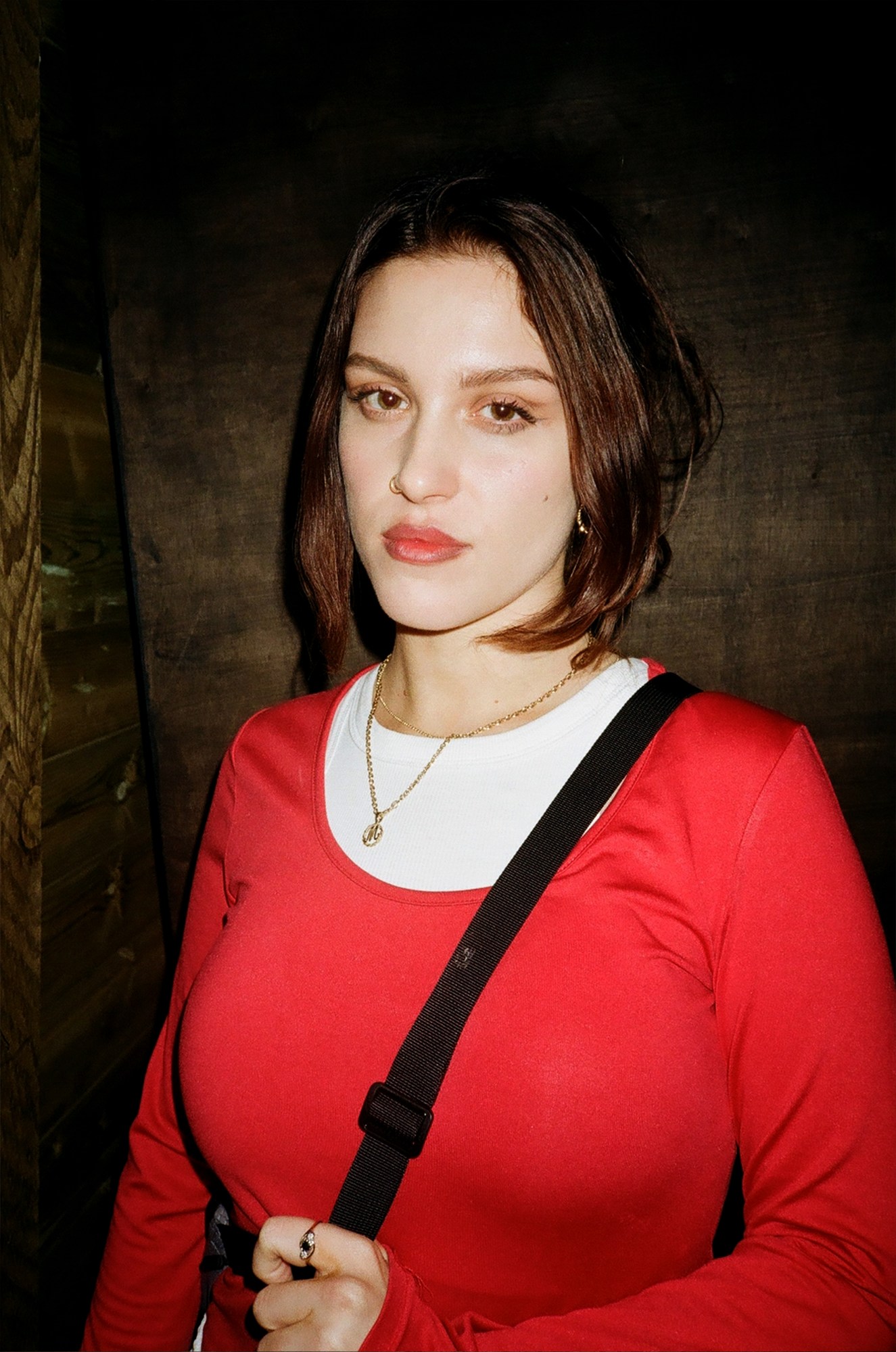 a girl in a red t-shirt with a nose piercing looks to camera