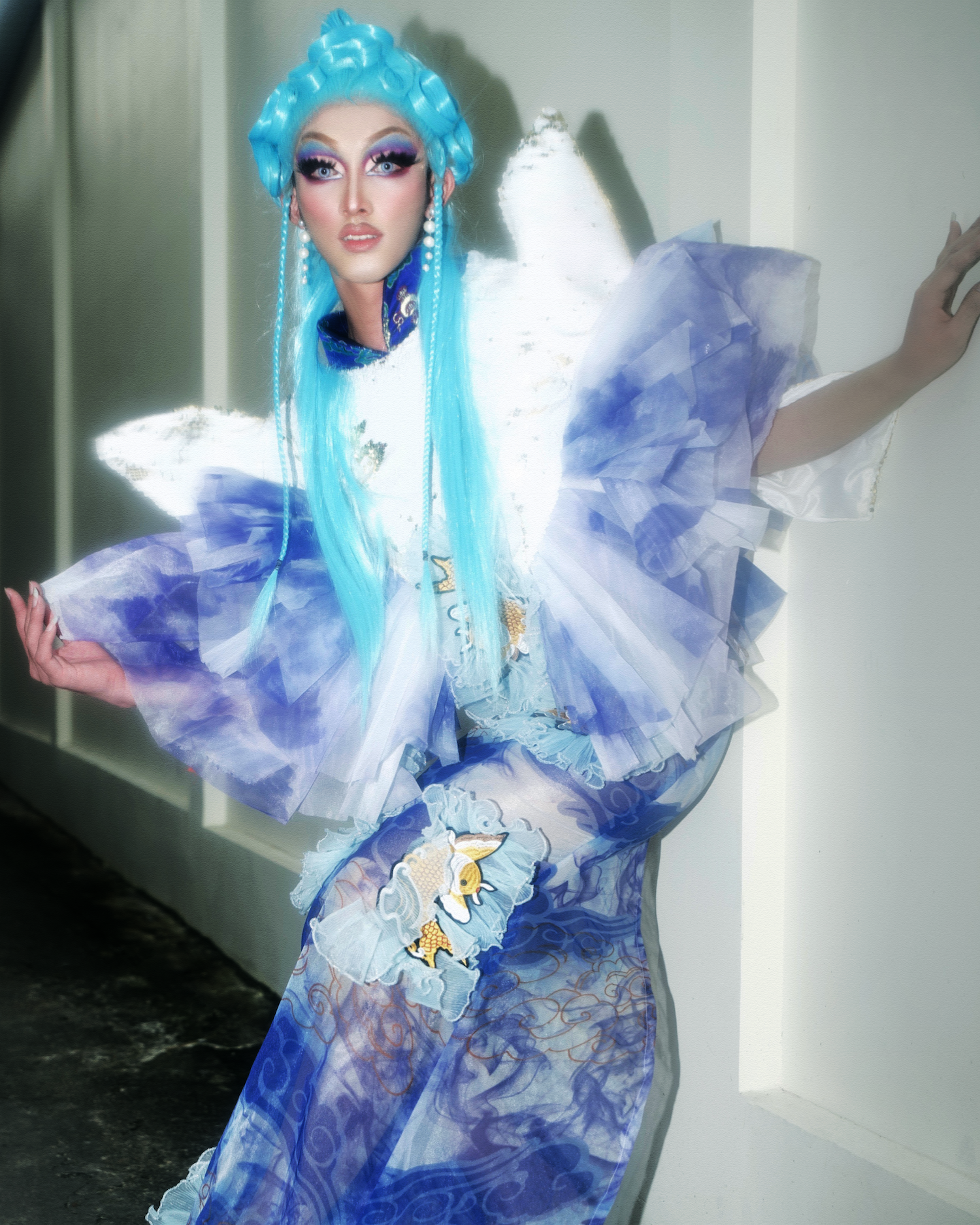 vietnamese drag queen harley posing against a wall in a blue outfit