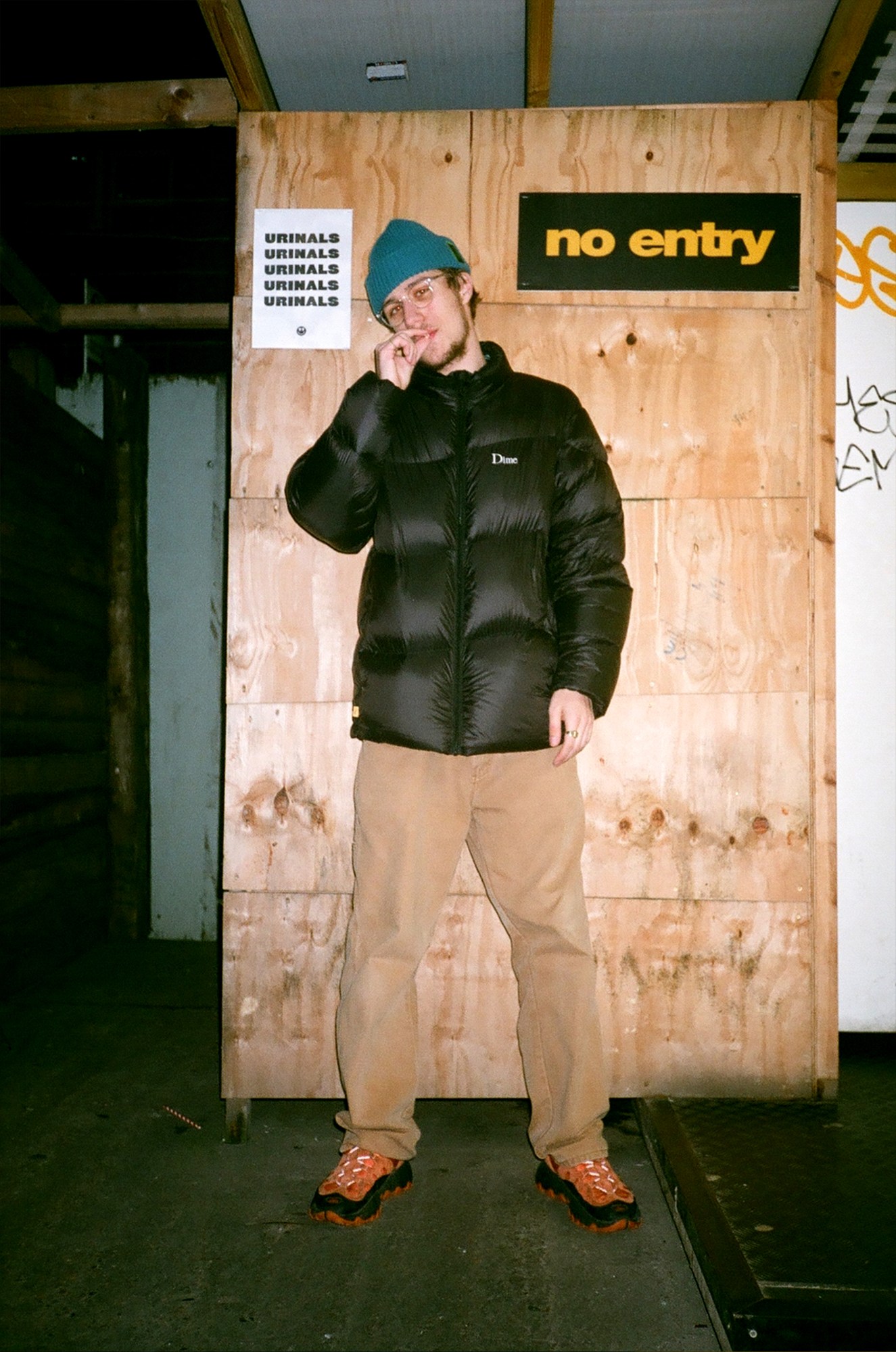 a guy in a puffer jacket and beanie takes a drag of his cigarette, looking to camera