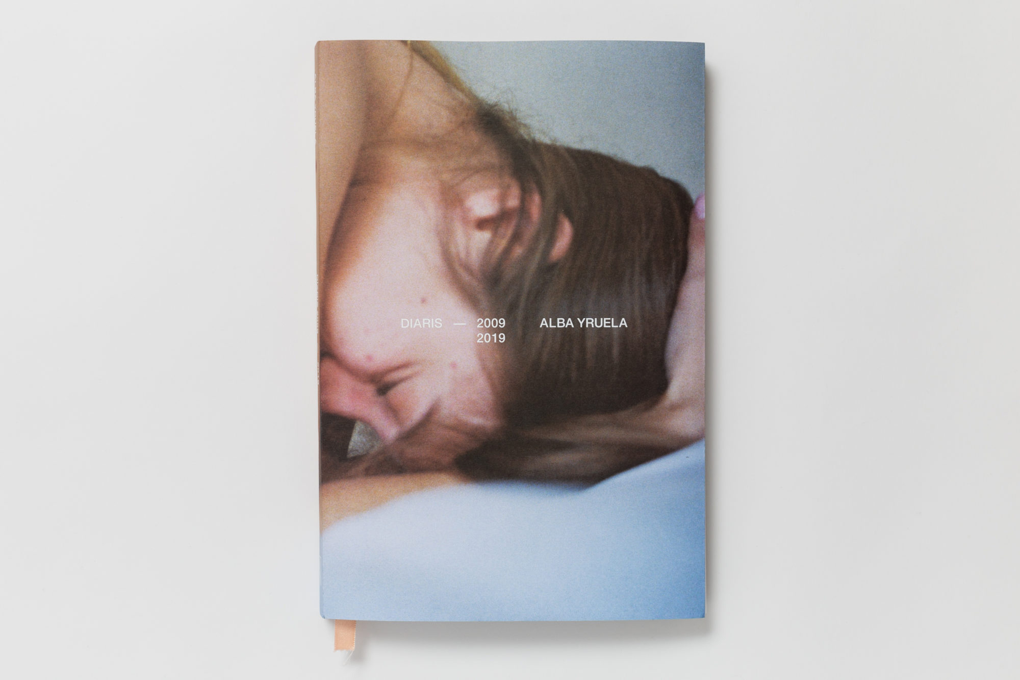 the cover of diaris 2009-2019, a side profile shot of woman holding her head in her hands, pressing into a bed