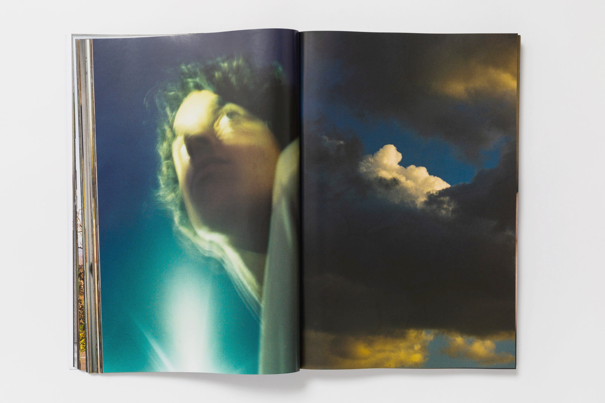 a double page spread from the book: left is a blueish blurry photo of a curly-haired model's face, taken from below; right is a picture of dark clouds on an otherwise sunlit sky