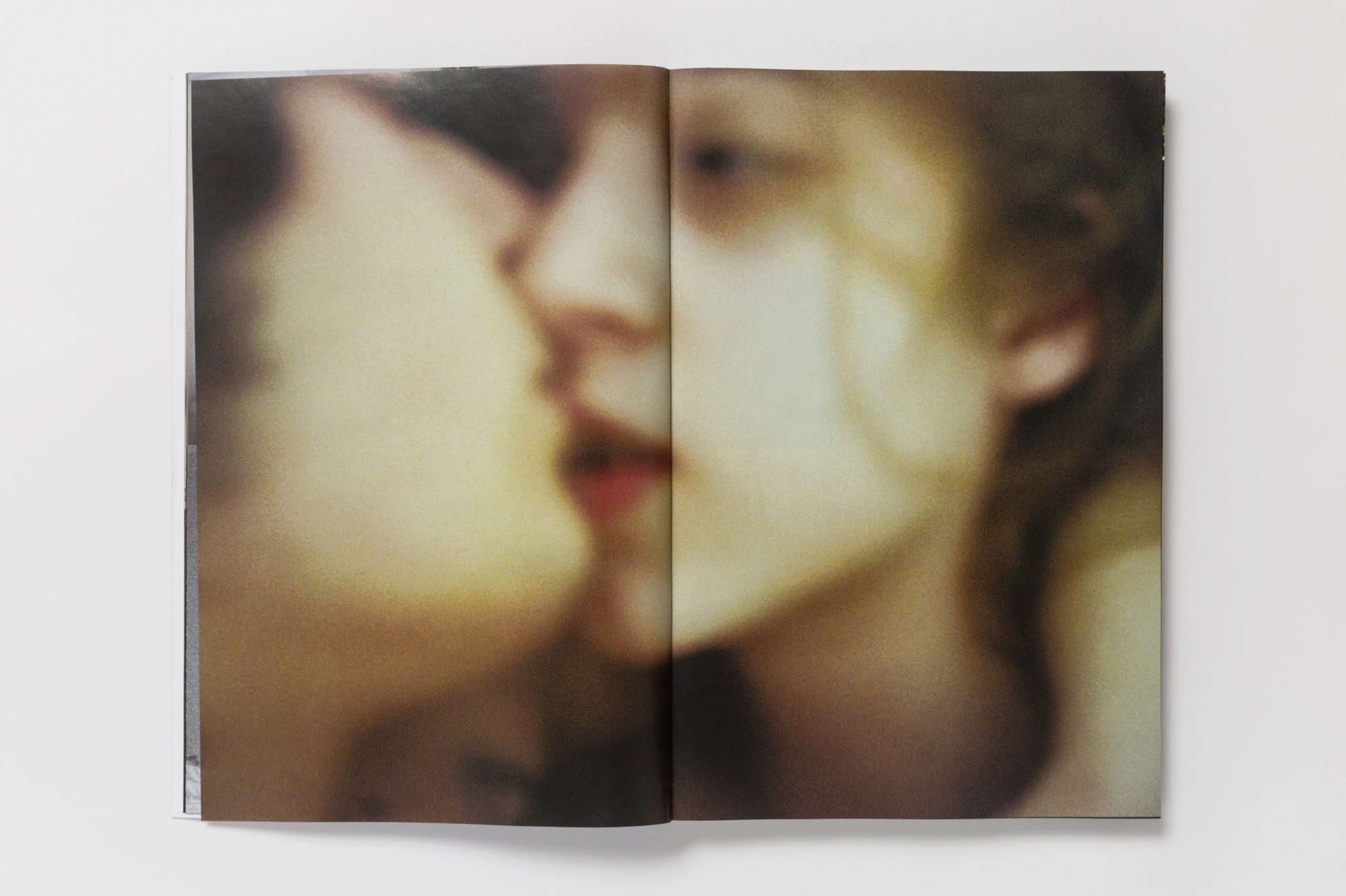 a blurry close-up double spread of two faces pressed together, lovers in embrace