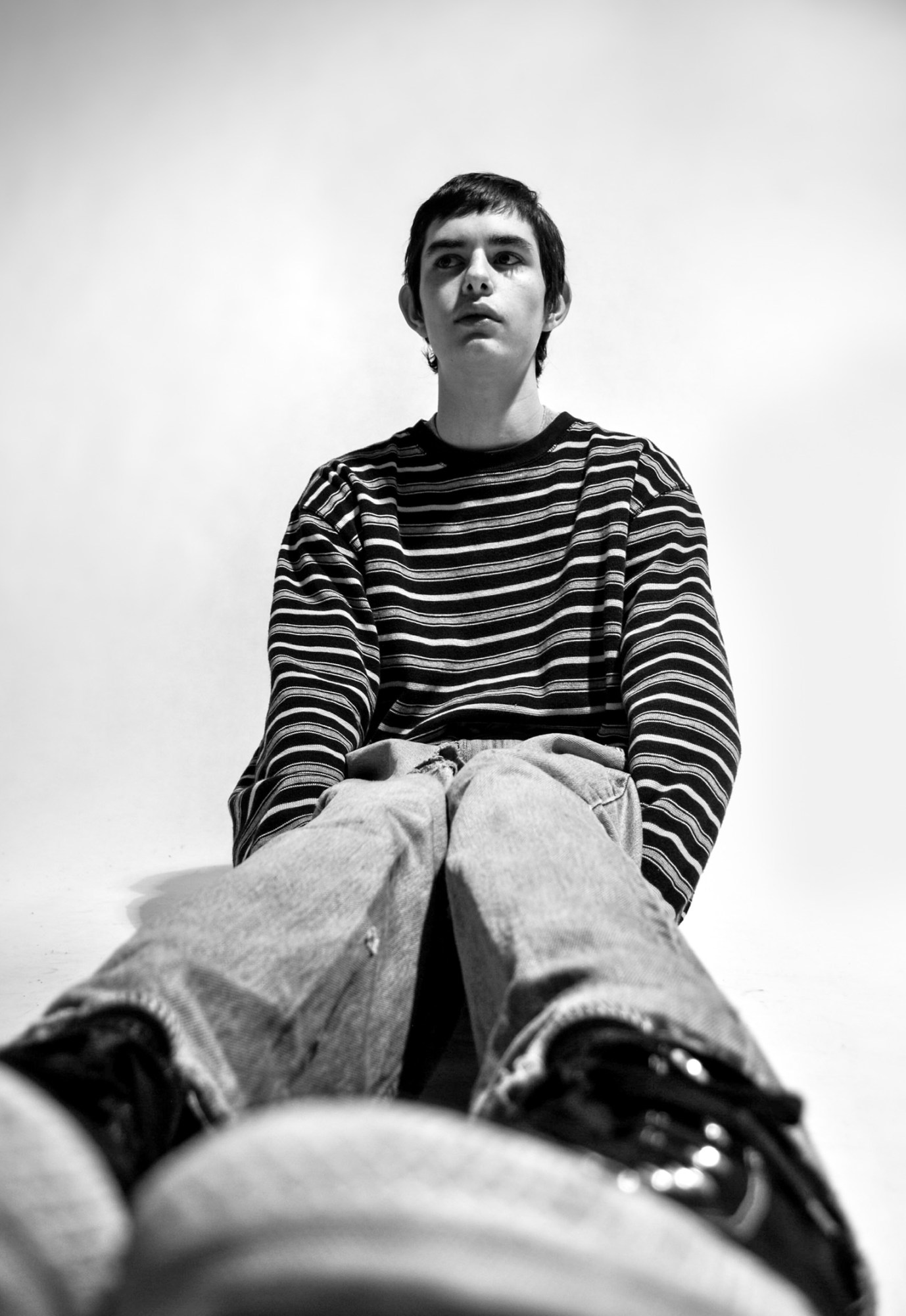 a young man in a stripy top sits on the floor of a studio