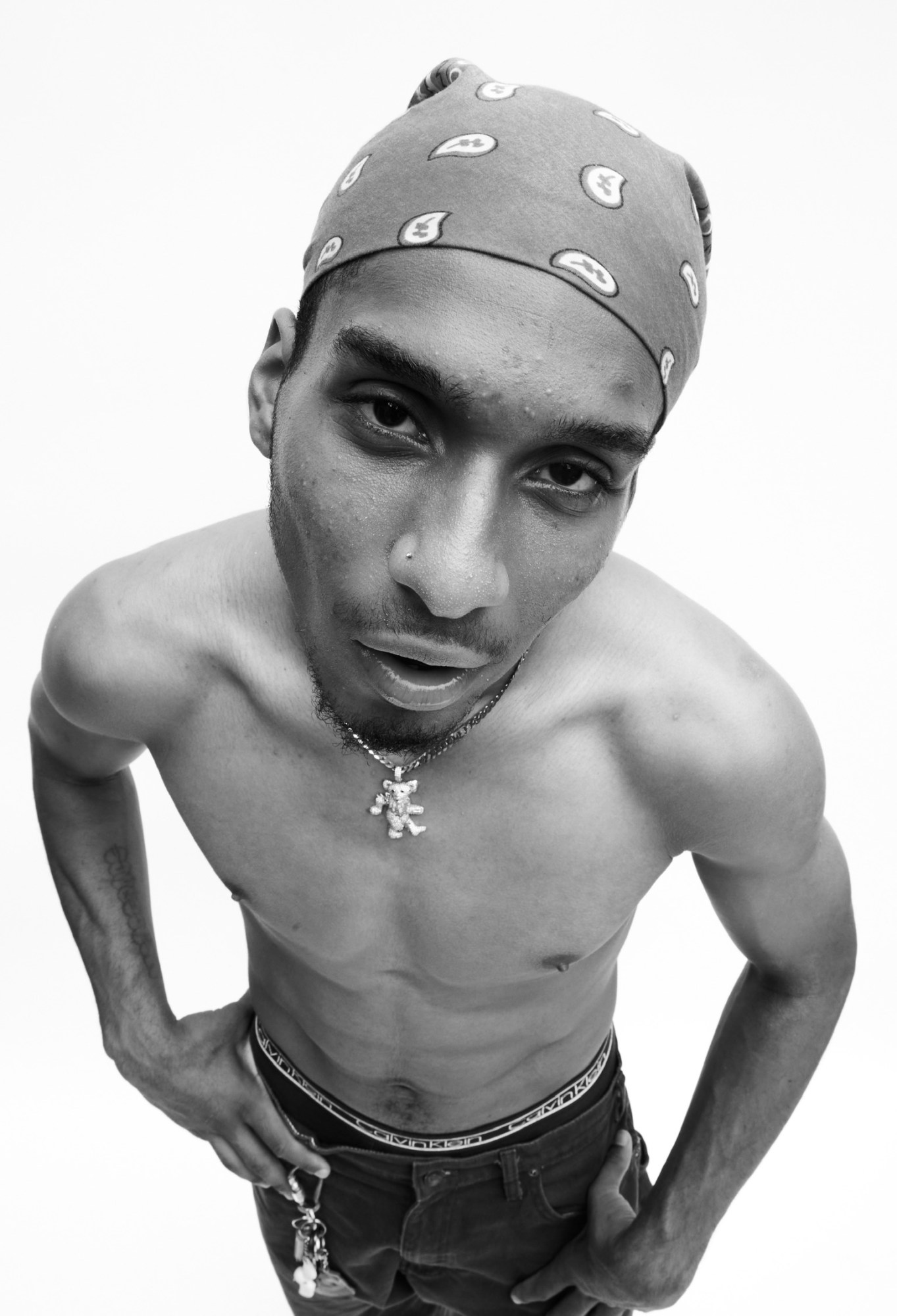 a topless man wearing a bandana looks up at the camera