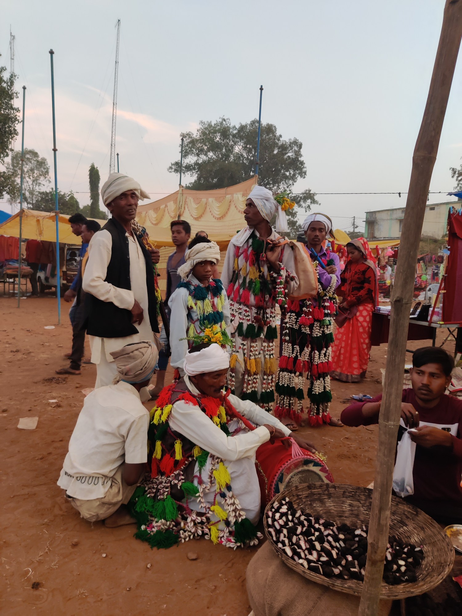 Men in colourful garments hold drums while sitting and standing on the side of a road.