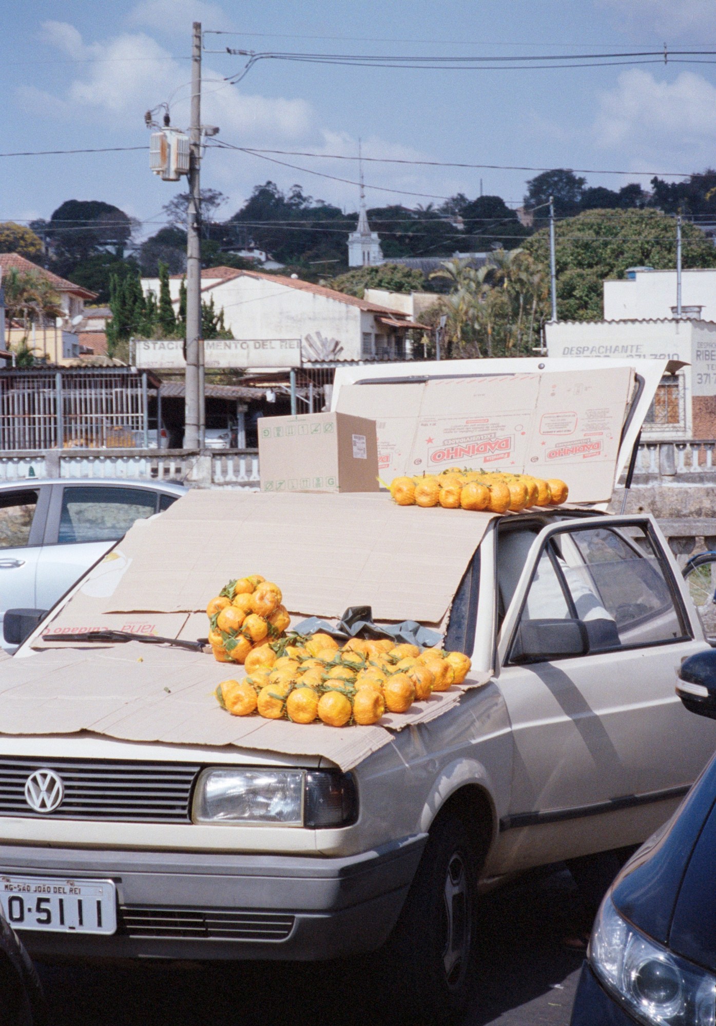 A car covered by cardboard and nets of oranges.