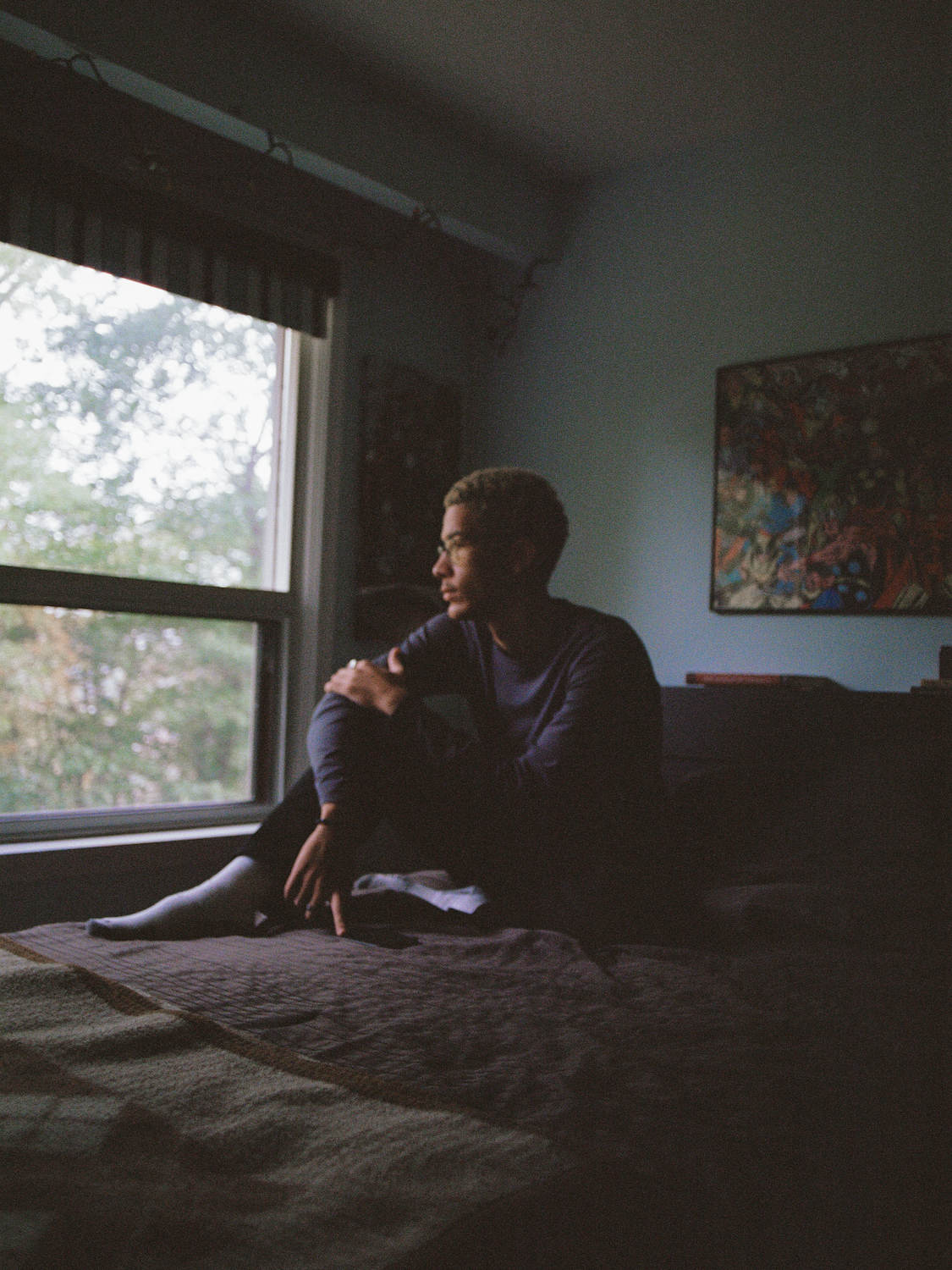 A boy sits on his bed staring out of the window.