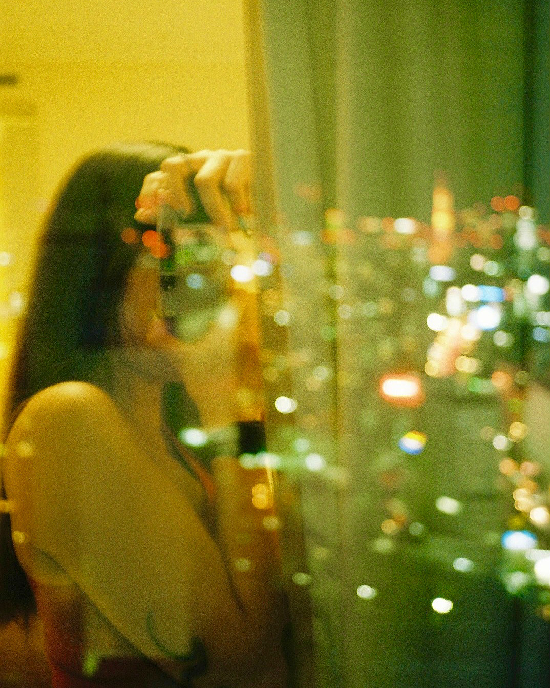 A girl takes a selfie in the reflection of a wet window with the colourful lights of the city outside glowing through the pane.