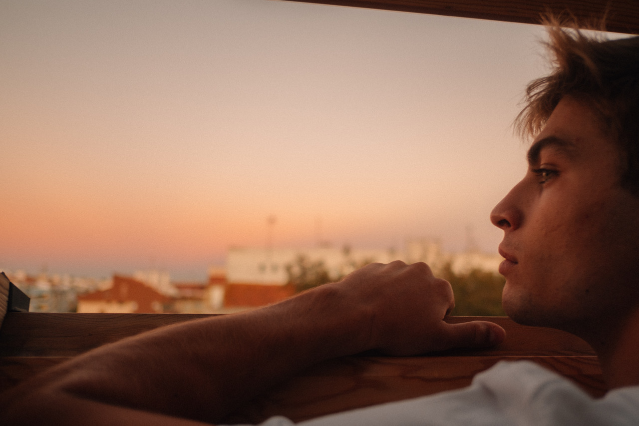 A boy looks thoughtfully out of the window as the sun begins to set.