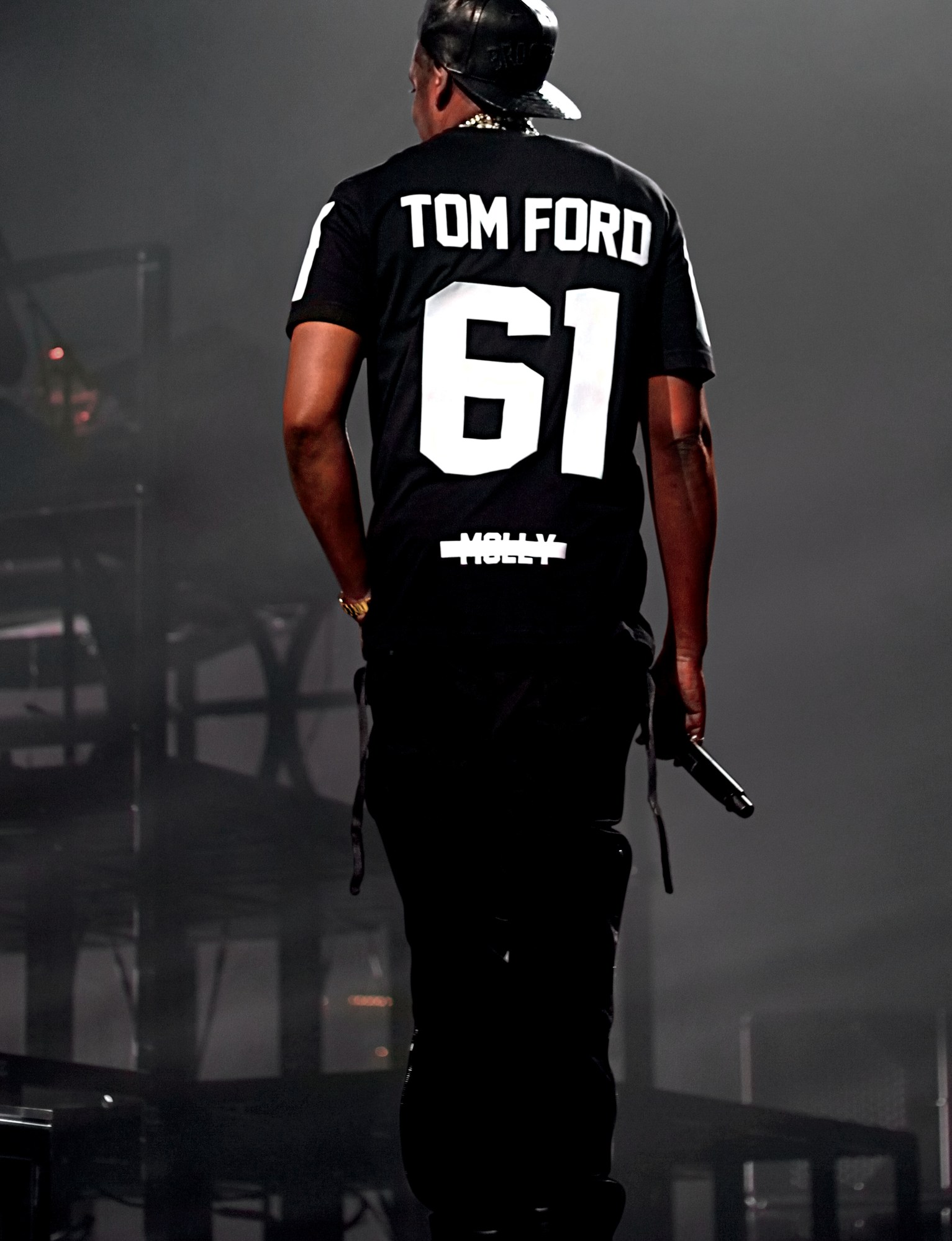 Jay-Z standing with his back to the camera on a stage. His top says TOM FORD 61 MOLLY.