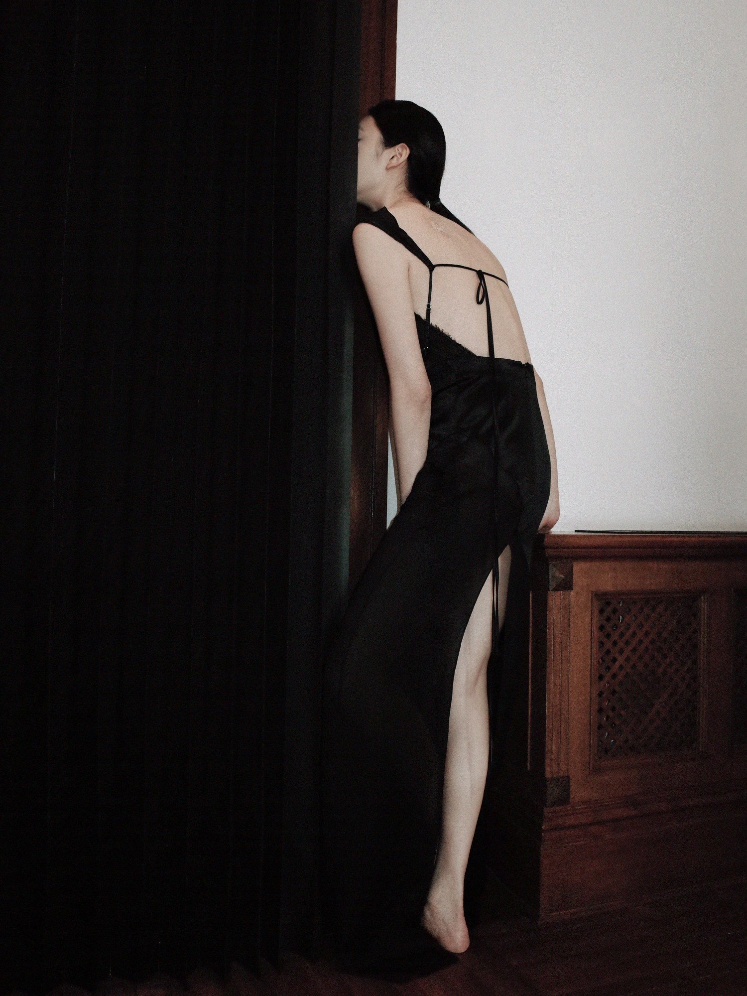 A model wearing a long black Peter Do dress, with her face hid behind a curtain