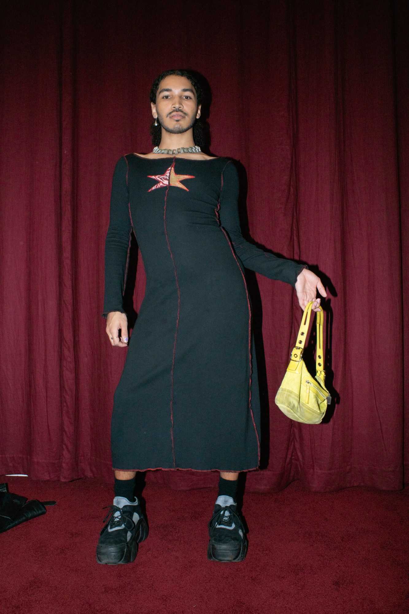 a person in a 90s style dress and platform buffalo trainers poses holding a yellow saddle bag