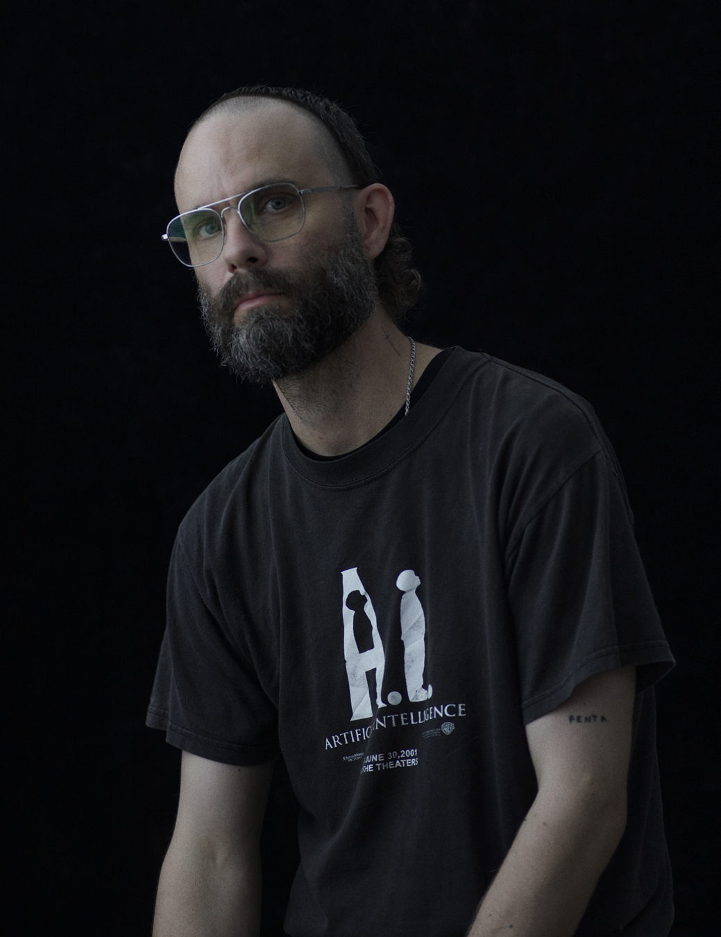 John wears a black t-shirt saying Artificial Intelligence and large silver glasses.