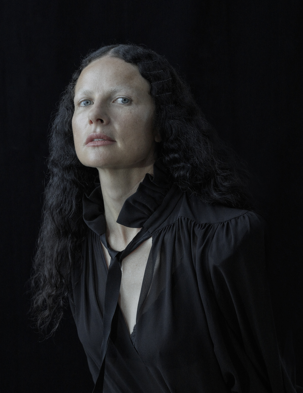 Isabelle wears a black tie front blouse and her black hair is crimped.