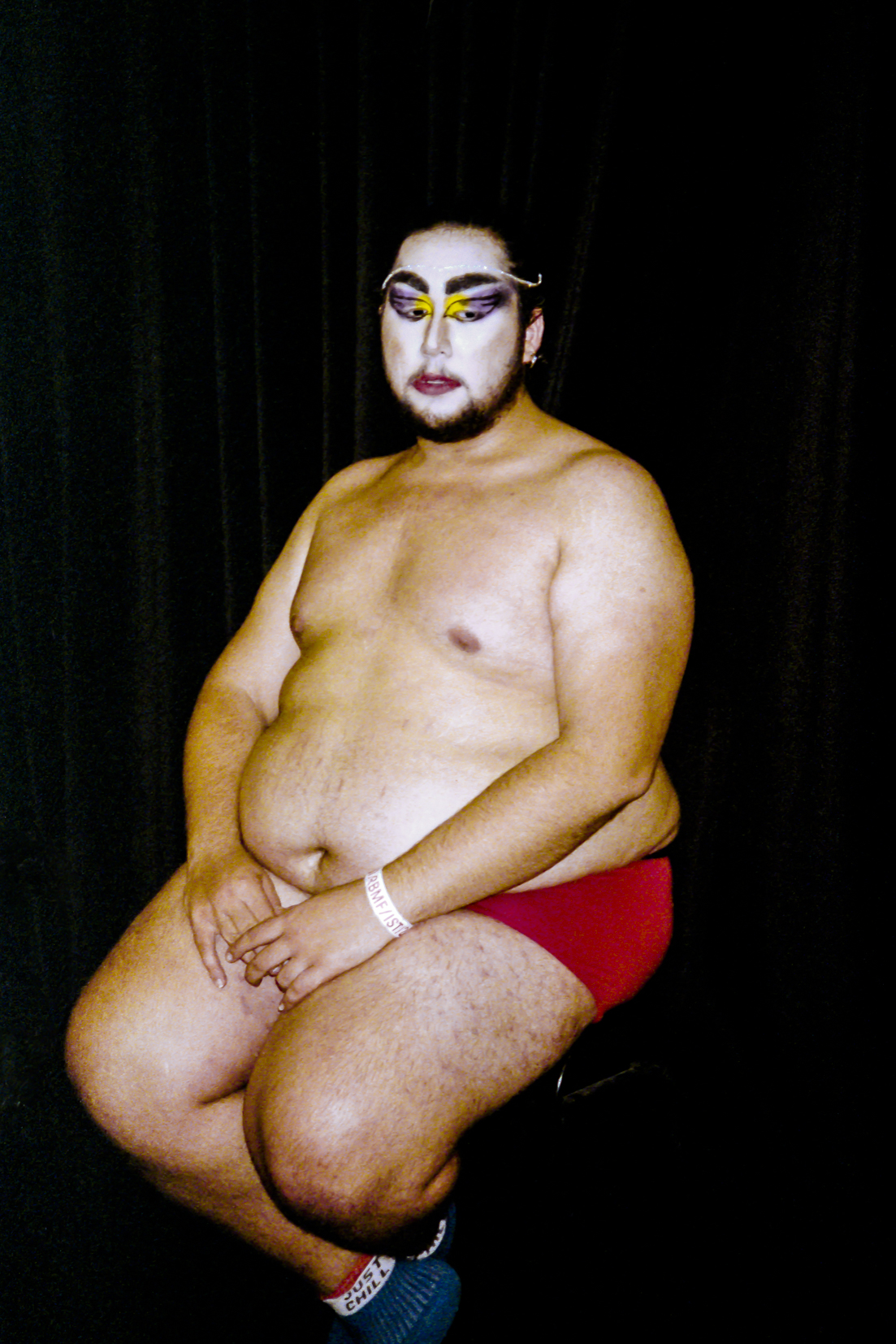 a man with face paint on sitting cross-legged on a stool