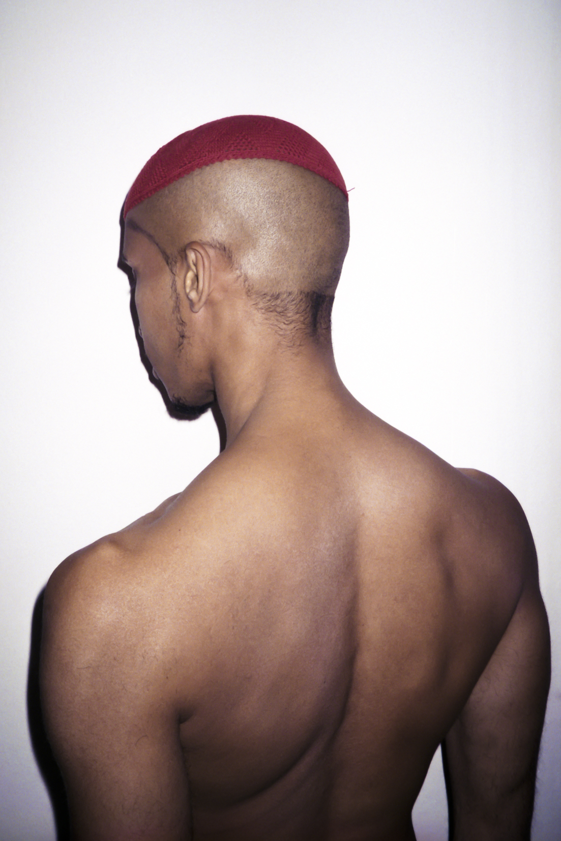 a man's back and shaved head wearing a red skullcap