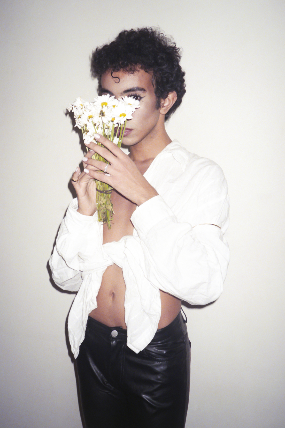 a man wearing eyeliner and holding up flowers to cover his face