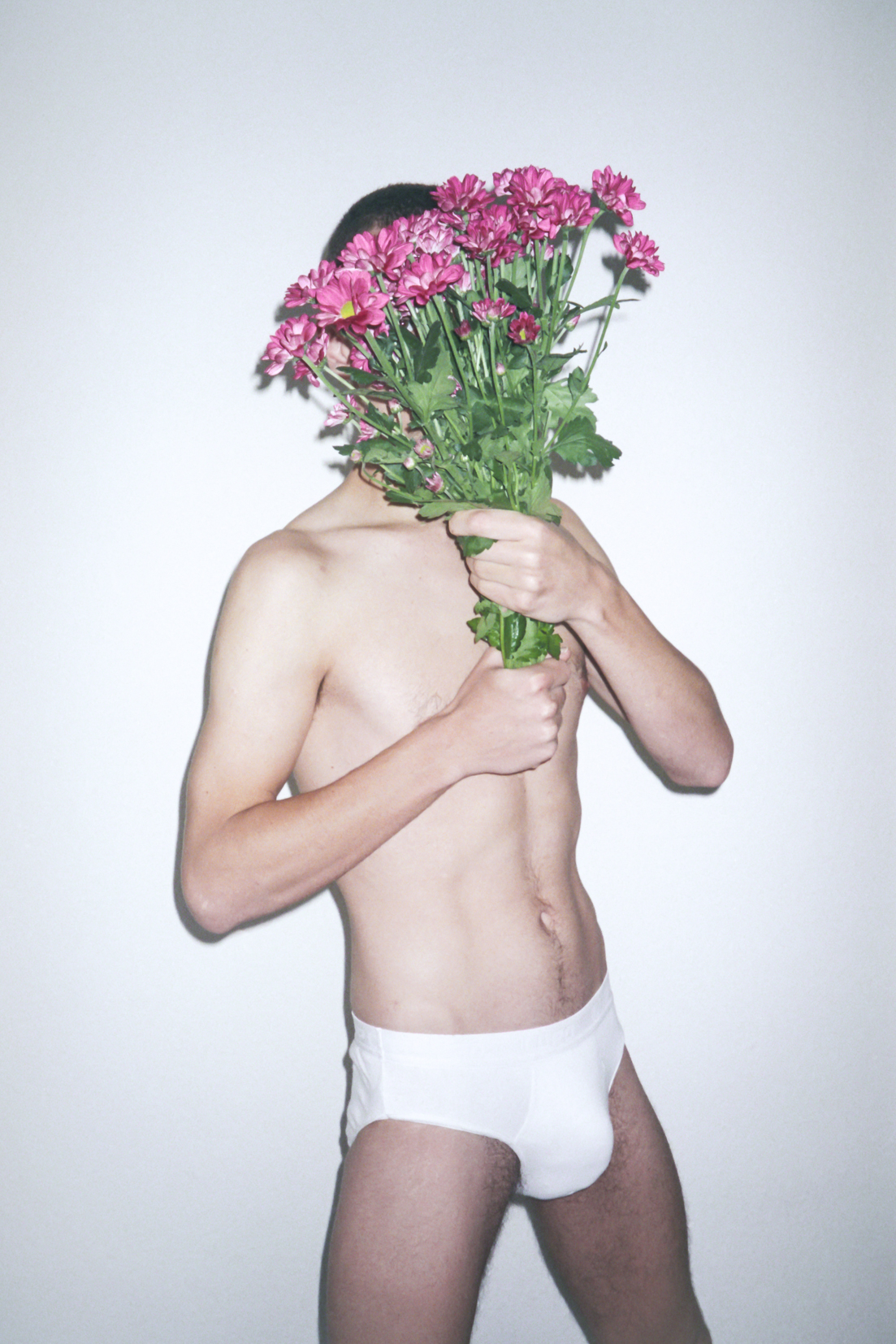 a man in white underwear covering his face with a bouquet of pink flowers