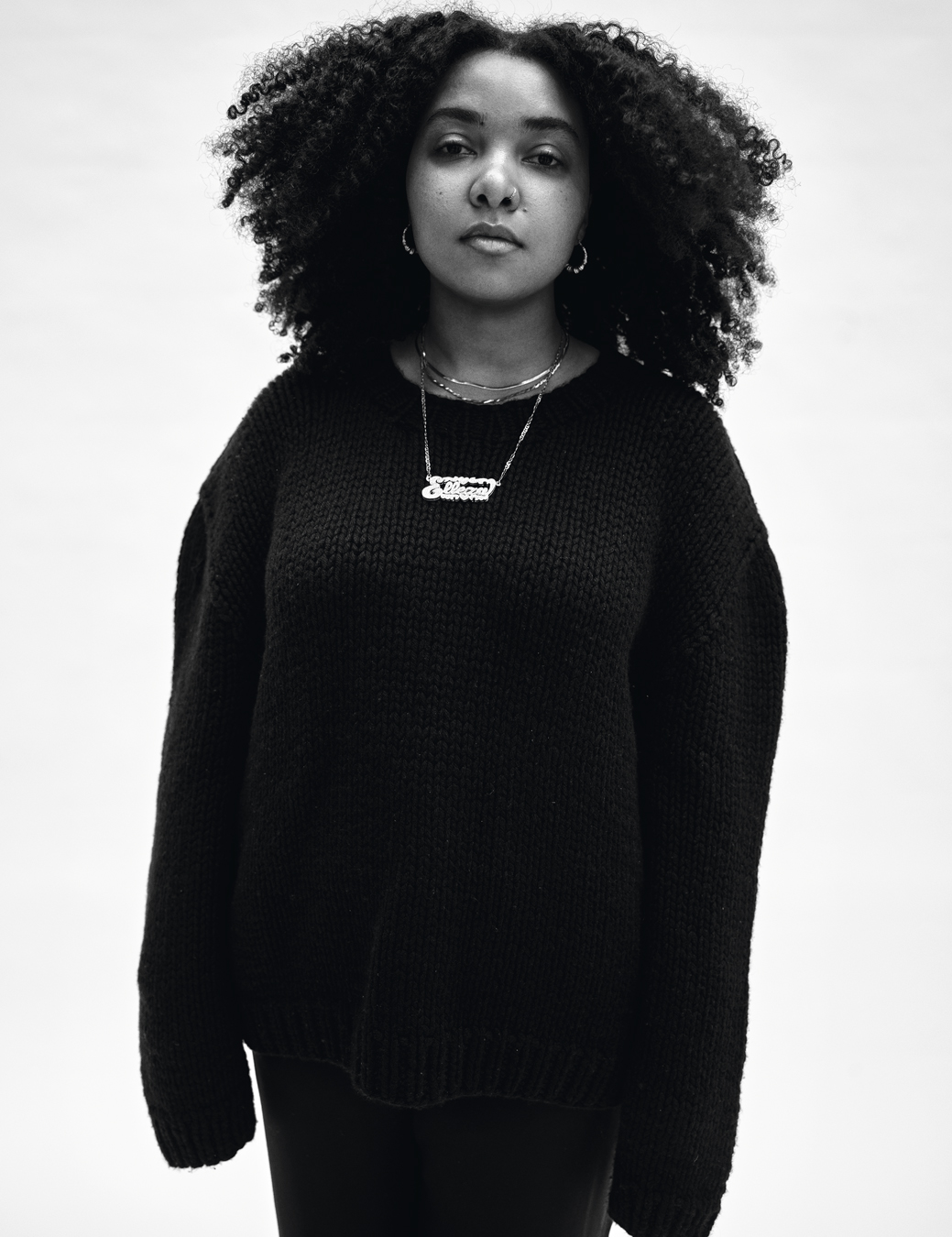 Elleza wearing a black long jumper with a lettered necklace