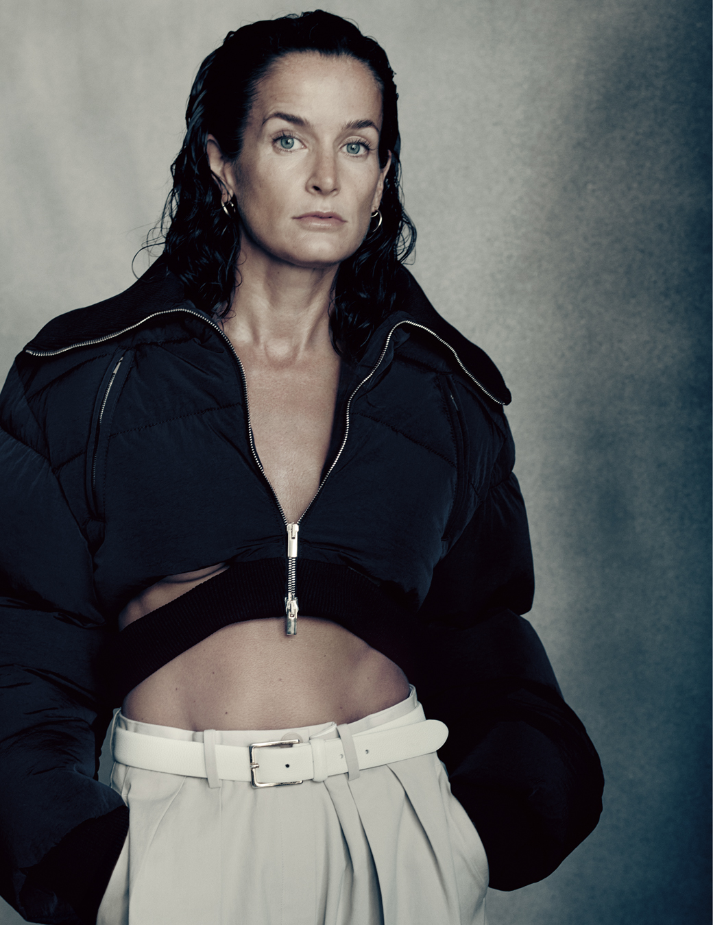 portrait of Lucy Chadwick wearing white trousers with a white belt, a navy cropped cut out hoodie and earrings.