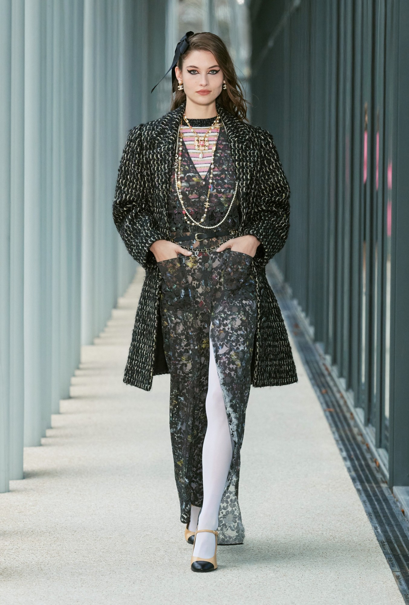 Model wears a floral sheer button up shirt dress with a pink and blue stripe top, white tights, two tone tan heels and a tweed coat.