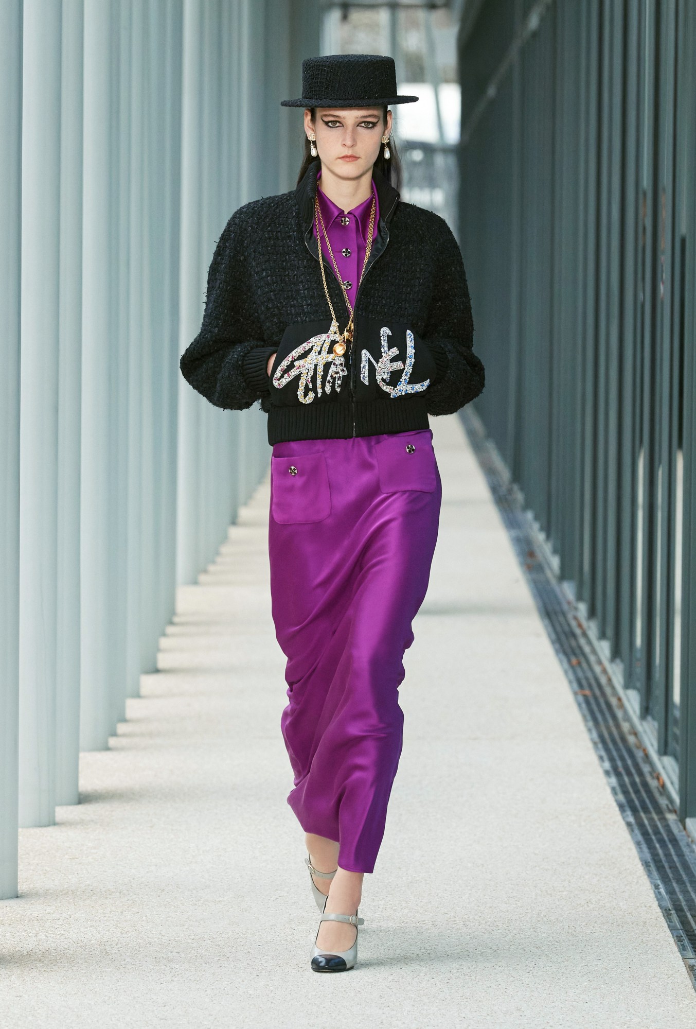 Model wears a purple satin dress with a cropped bomber jacket with CHANEL written across the front.