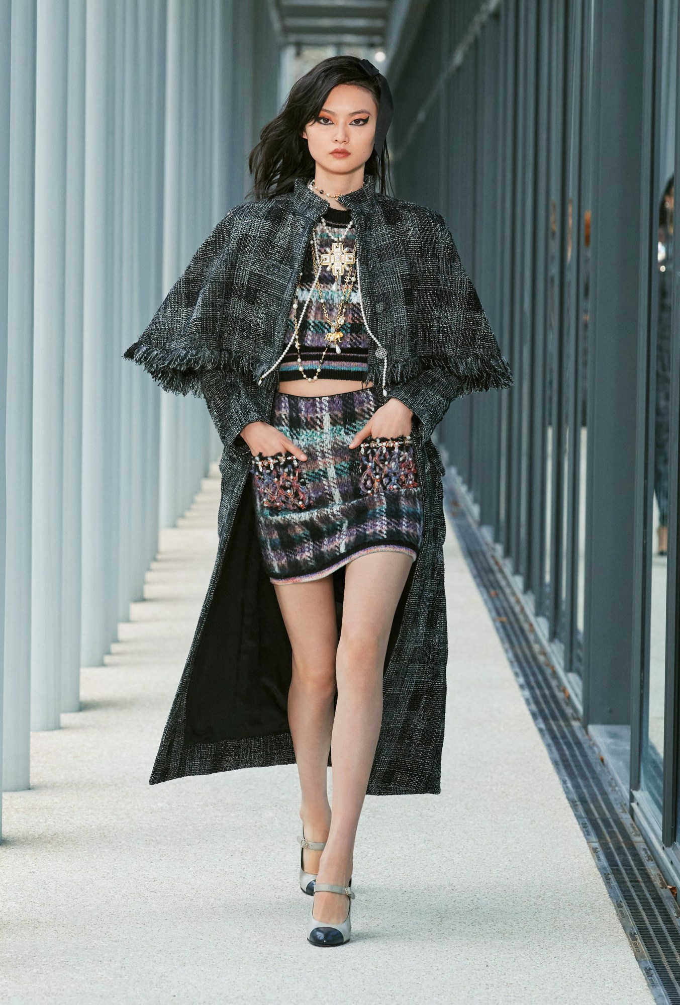 Model wears a two piece matching tweed skirt and top with a woven grey check overcoat.