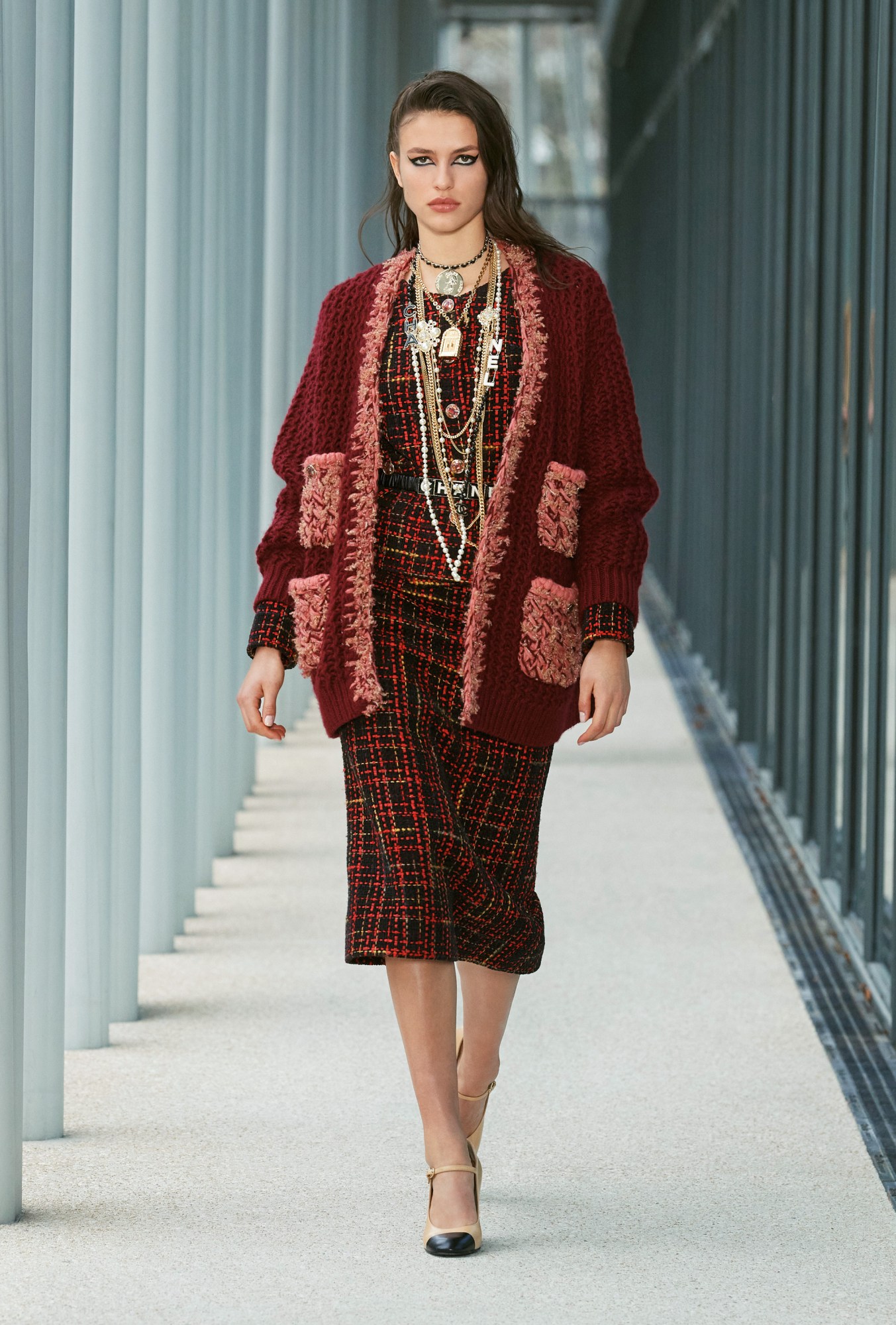 Model wears a tweed red dress with a red knitted cardigan and lots of necklaces.