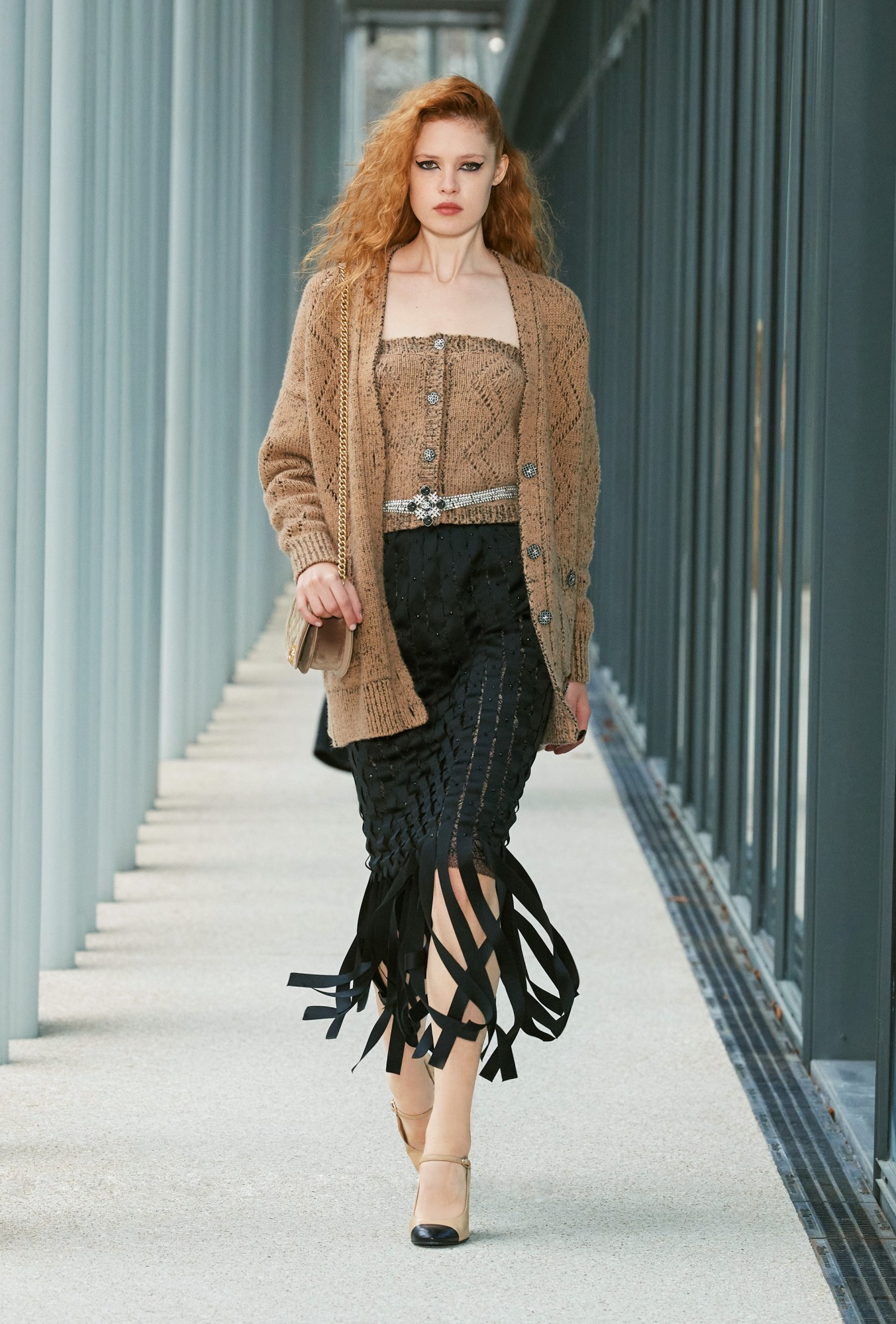 Model wears a knitted cardi top with a larger oversized cardigan and a fringed woven black skirt.