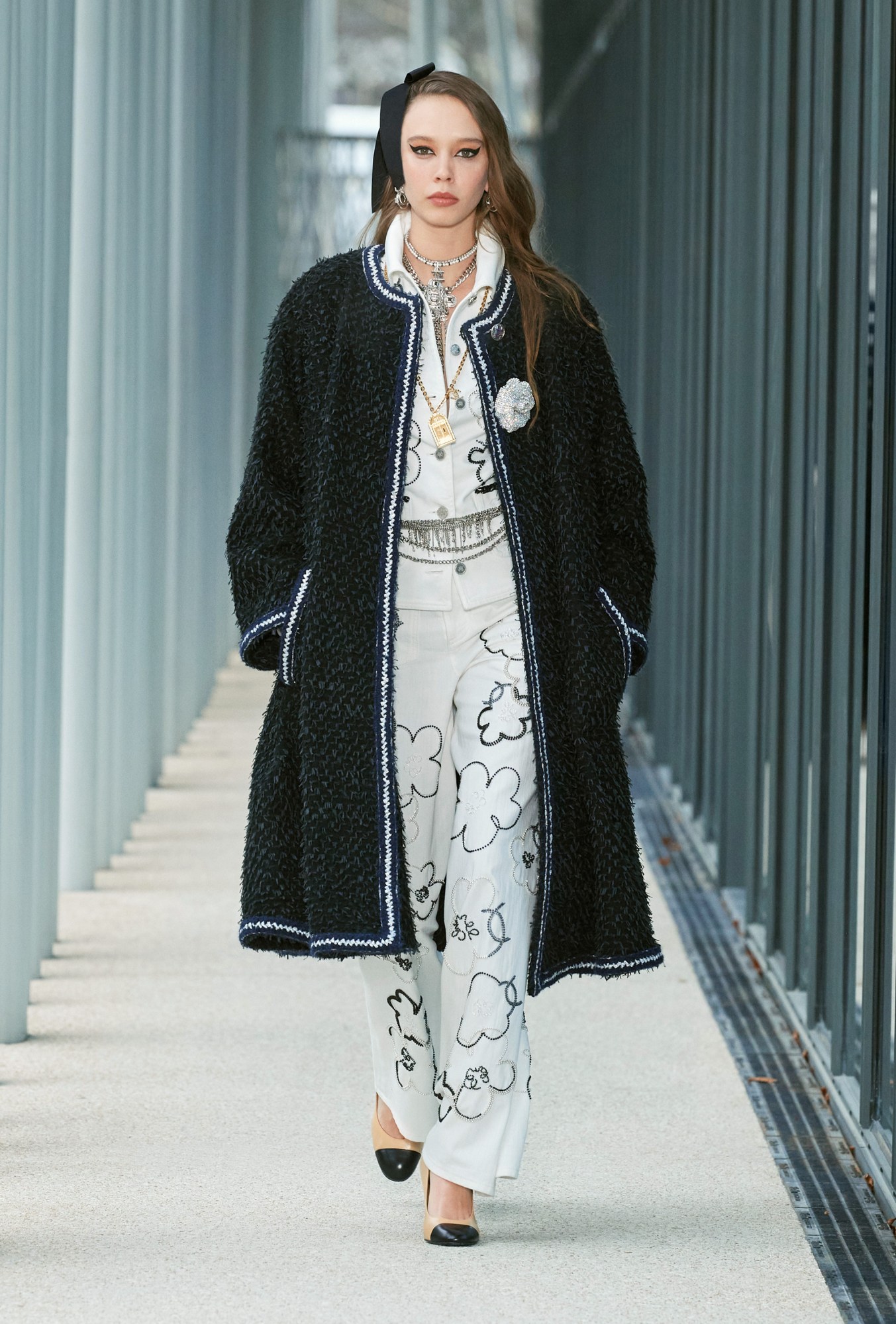 Model wears a matching cloud printed trousers and shirt combo with a black tweed overcoat and flower broach.