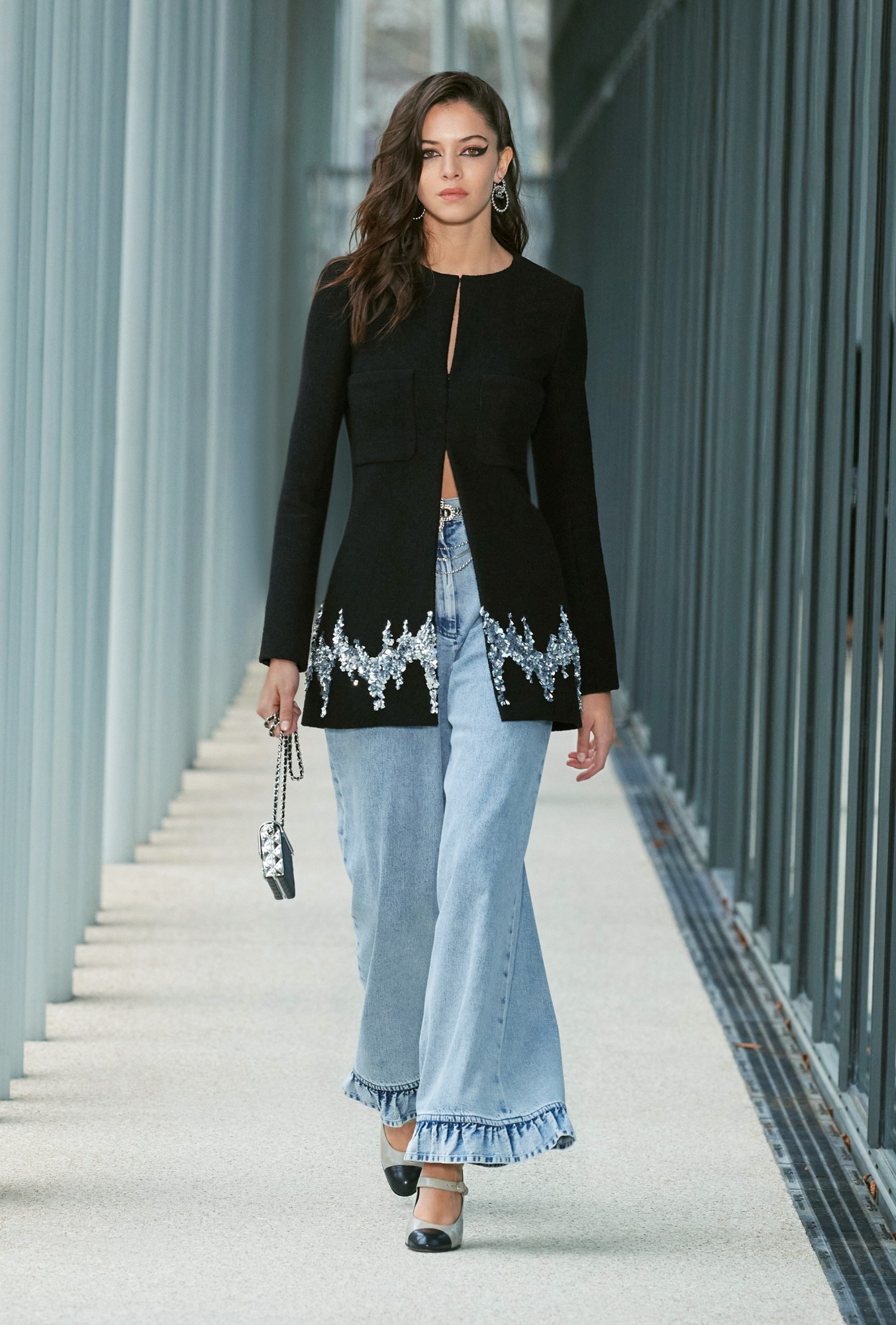 Model wears flared blue jeans with a black embroidered blazer.