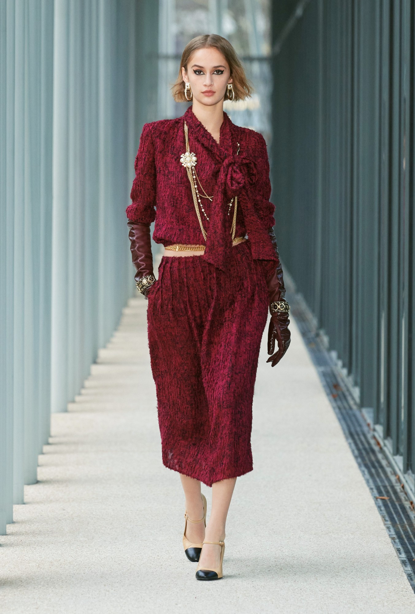 Model wears a red dress with leather glove accessories and gold necklaces and belt.