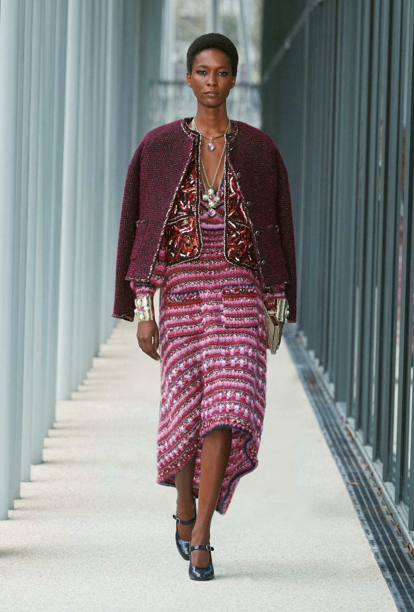 Model wears a pink tweed striped dress with two tailored red and purple jackets.