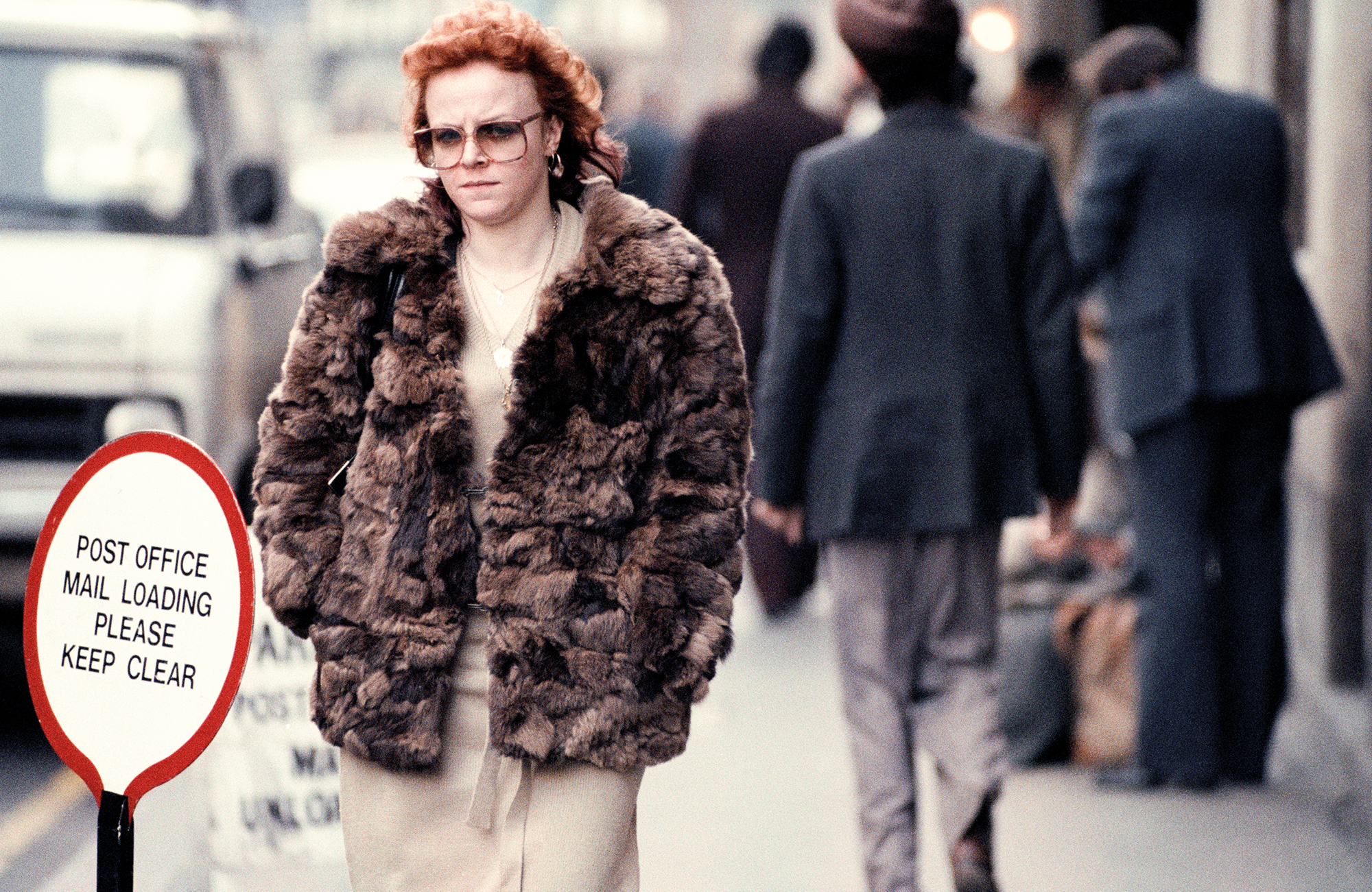 taken by sunil gupta in 80s london, a white woman with a curled ginger fringe and a fur coat walks down the street