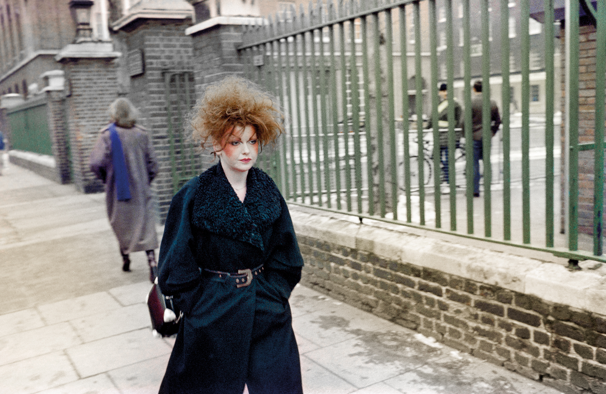 taken by sunil gupta in 80s london, a white woman with combed-back hair and new romantics hair walks down the street