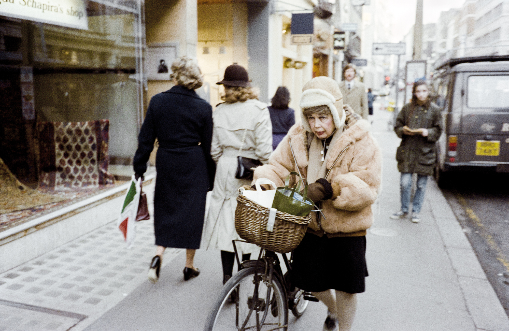 taken by sunil gupta in 80s london, an elderly white woman with a bike wears a cropped fur coat and a hat