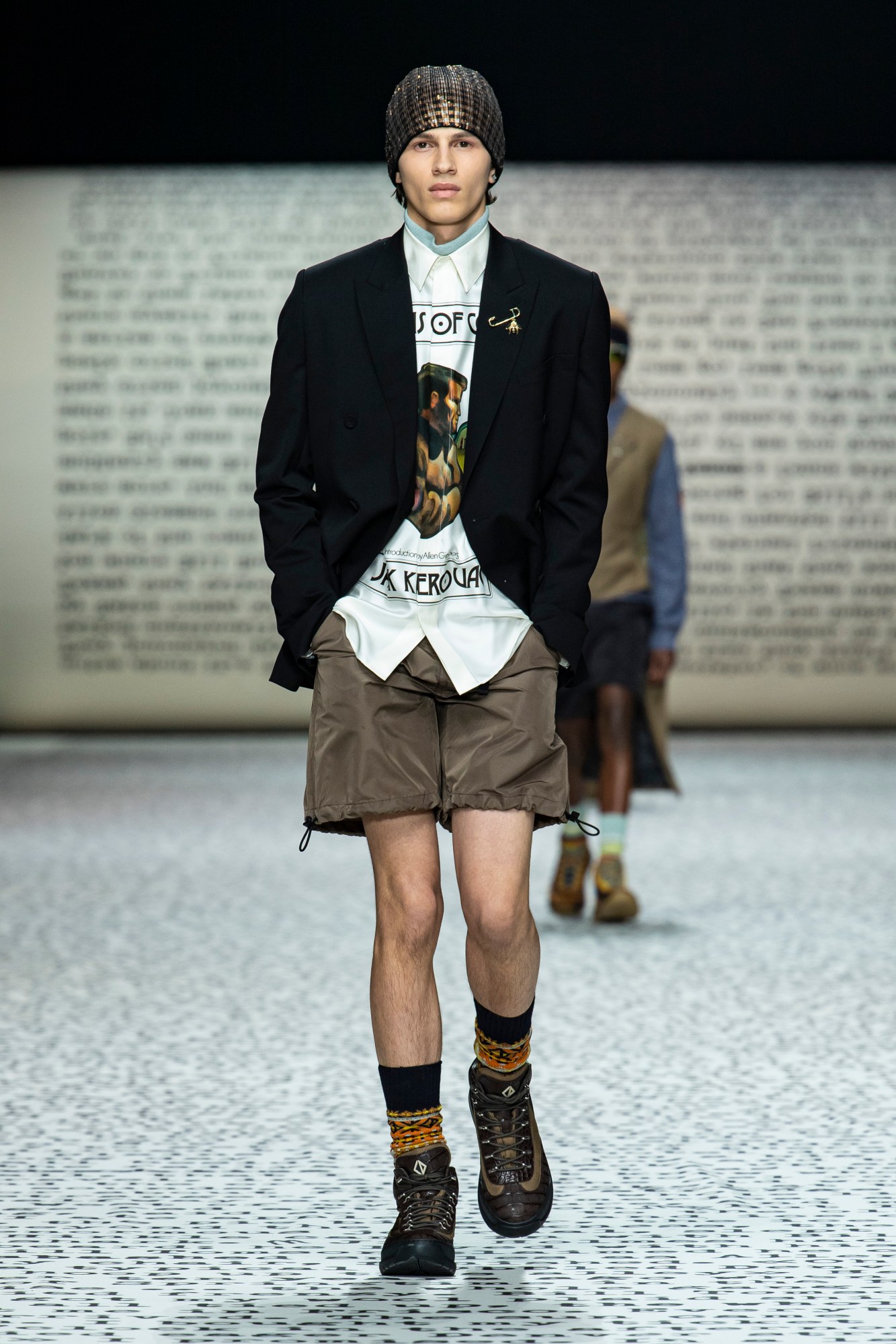 Model wears cargo shorts with a printed shirt, black blazer, walking boots and fair isle socks