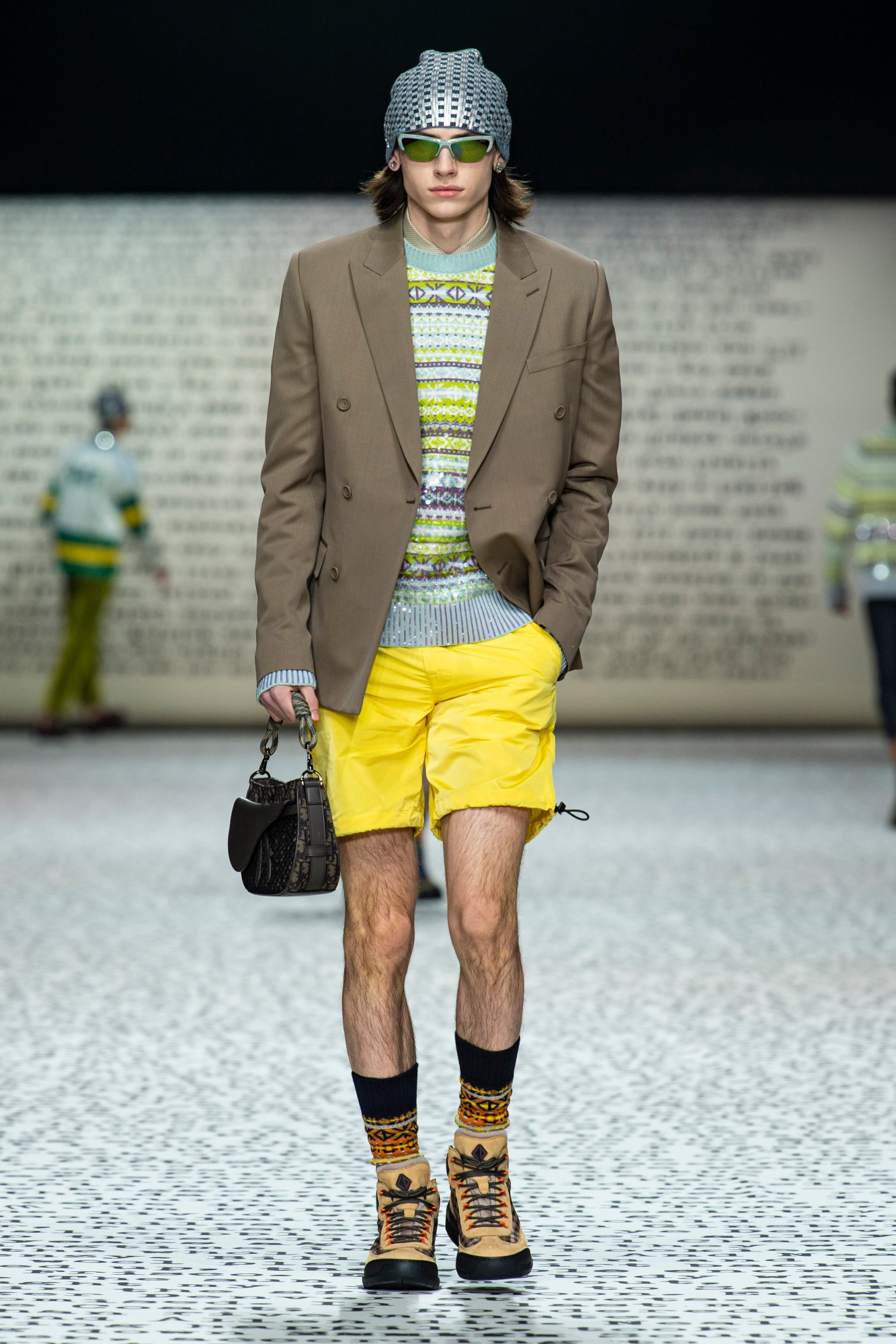 Model wears yellow cargo shorts with a fair isle jumper and a brown blazer with cream walking boots and a fair isle socks.