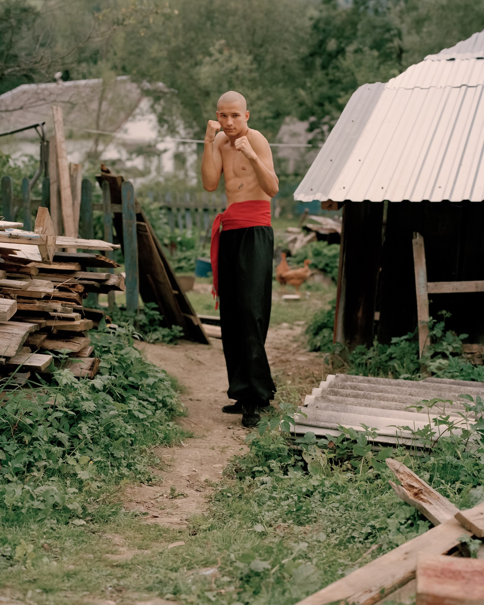 a topless man in black trousers holds his fists up