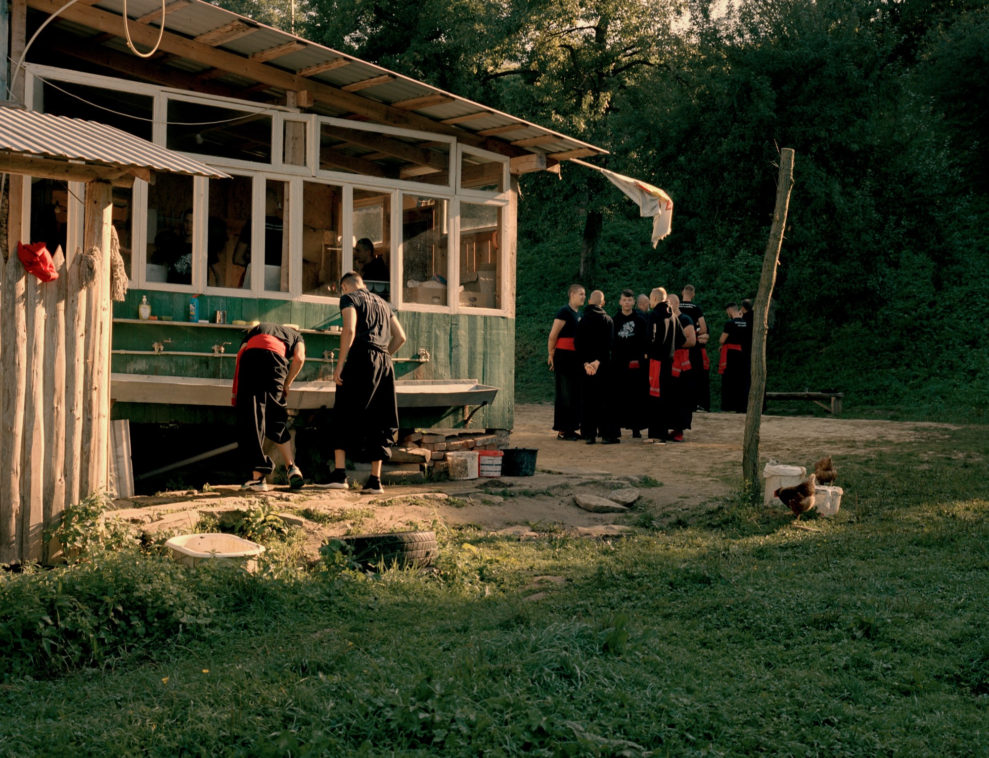 young men congregating around a hut in a wooded area