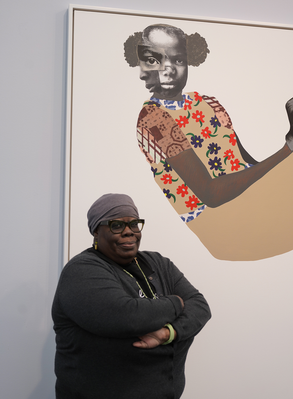 Deborah Roberts stands in front of her painting of an abstracted collaged face of a young black girl.