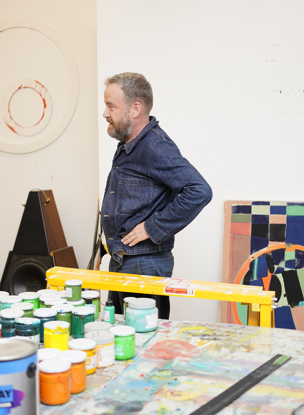 Matt Connors in double denim standing in front of a painting station.