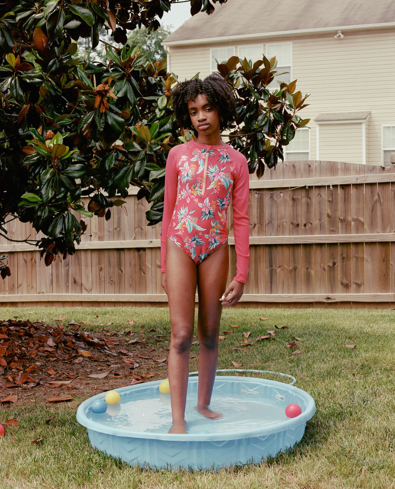 a girl in a long sleeve swimsuit standing in a kiddie pool outside by kennedi carter