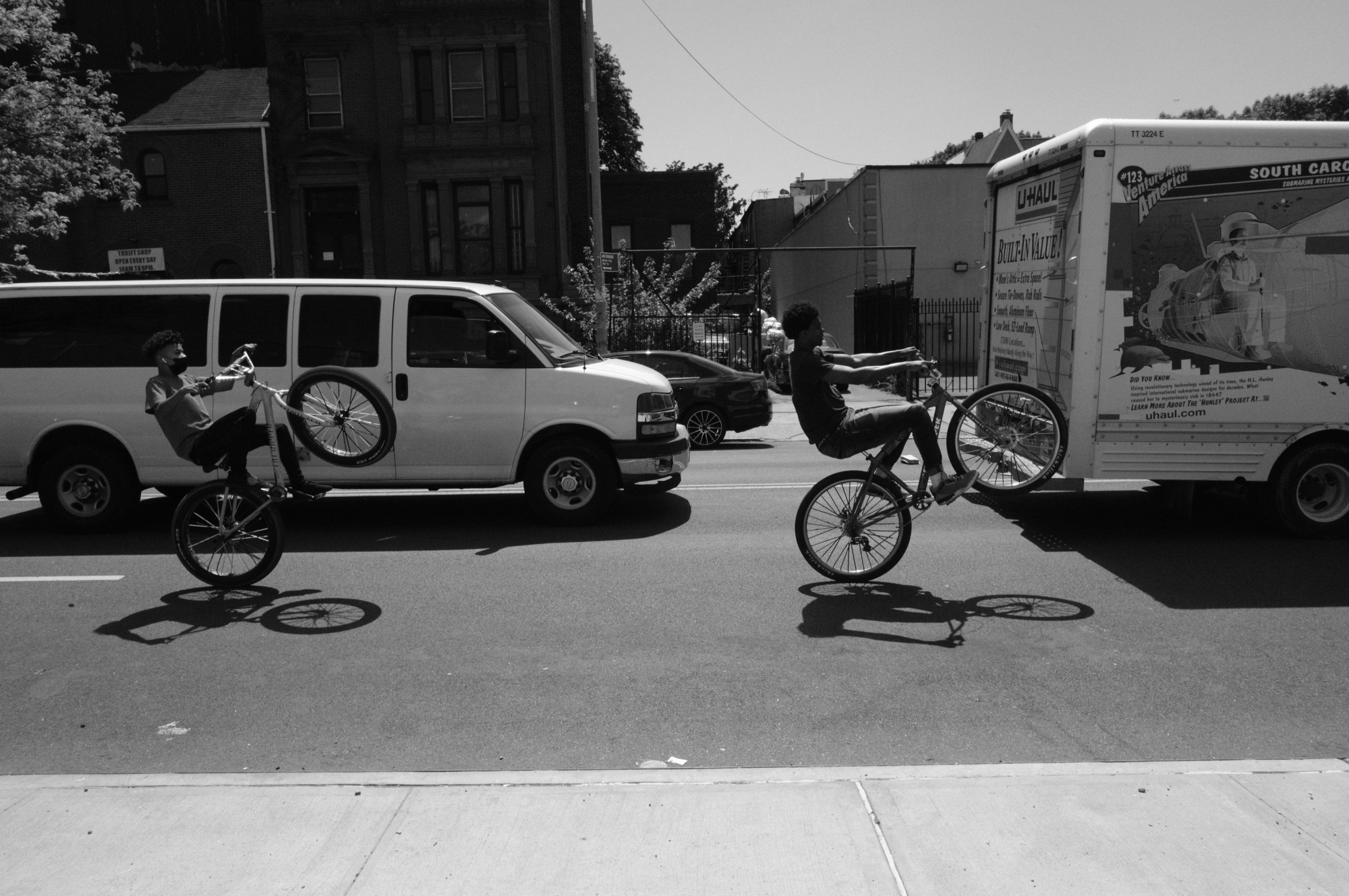 two bikers doing wheelies in front of cars in new york city by christopher currence