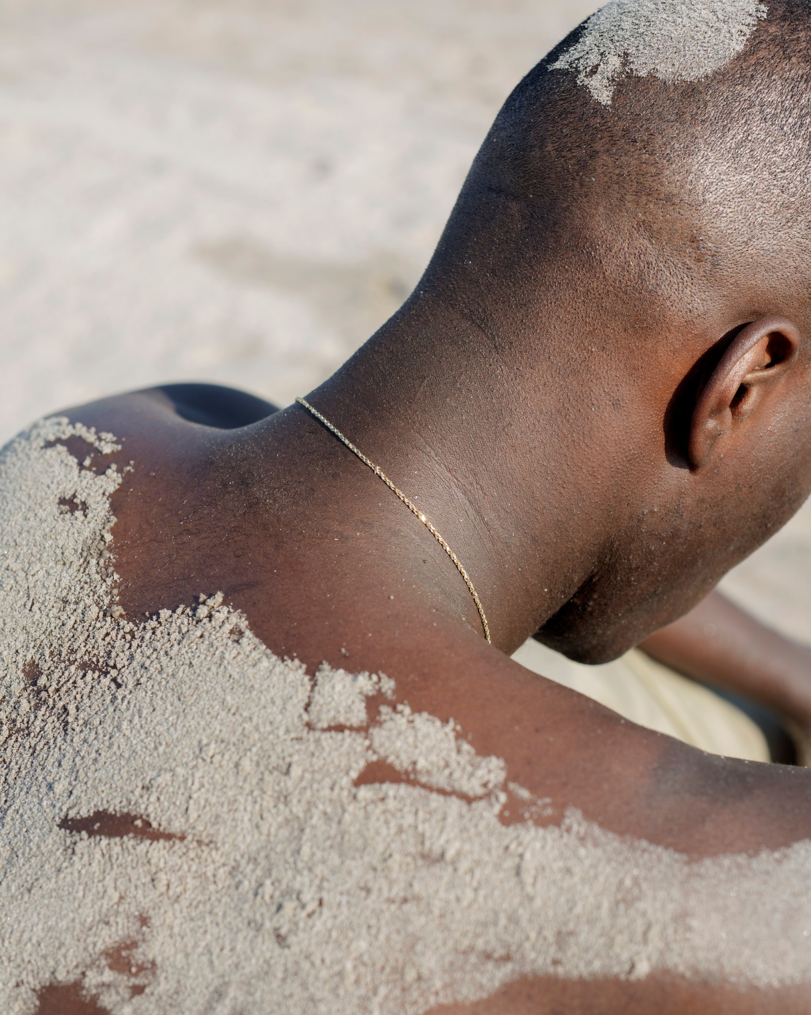 the back of a man's head and back covered in sand by jasmine clarke