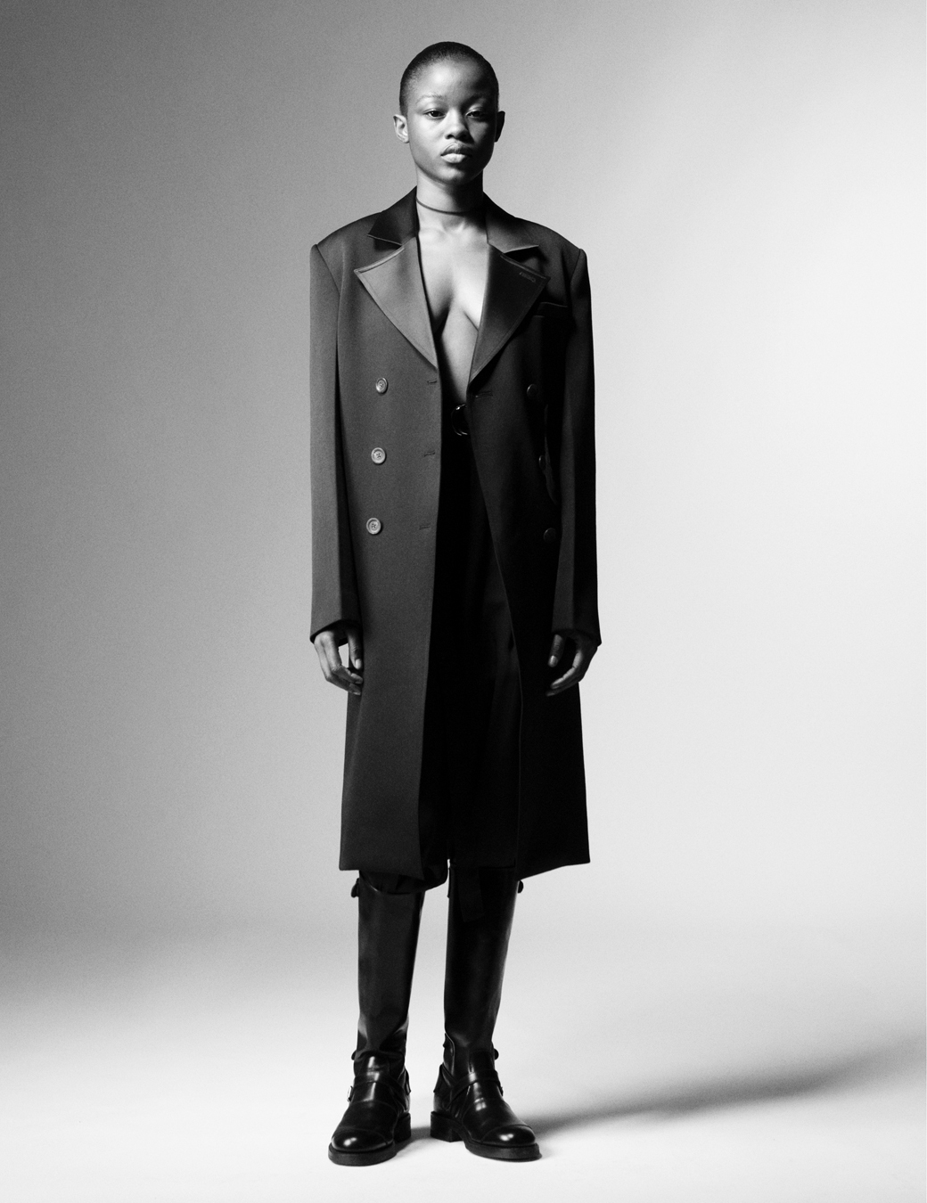 Model wears a black trench coat and black leather boots.