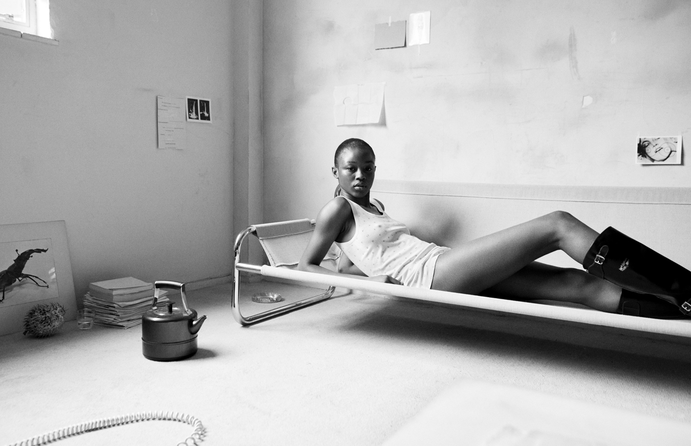 Model lying on a sofa in a derelict room wearing a vest and black boots.