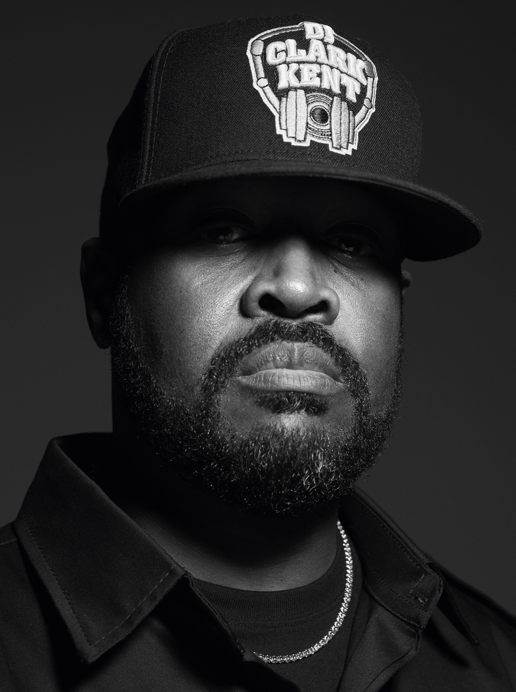 Portrait of DJ Clark Kent wearing a black shirt and tee and baseball cap with a diamond necklace.