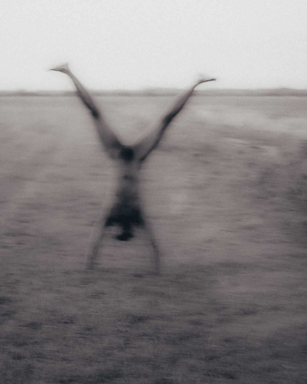 Blurry monochrome photo of a naked person doing a handstand.